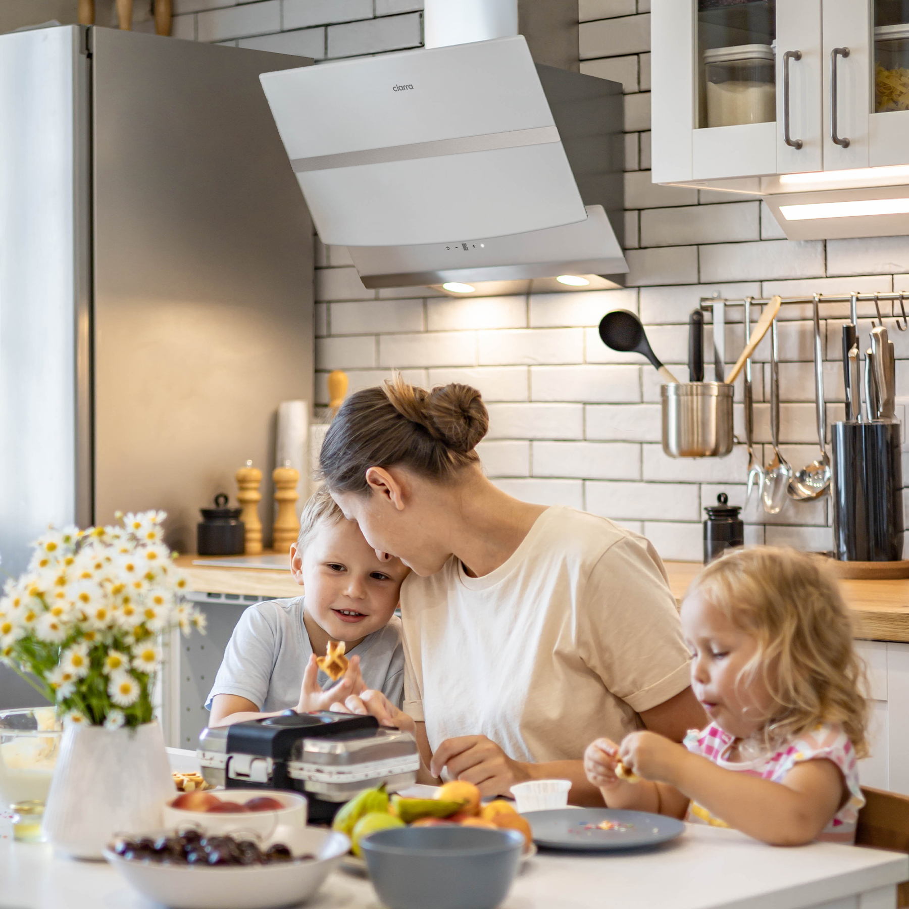 Familie in der Küche; Mutter und zwei Kinder, eines isst eine Waffel.