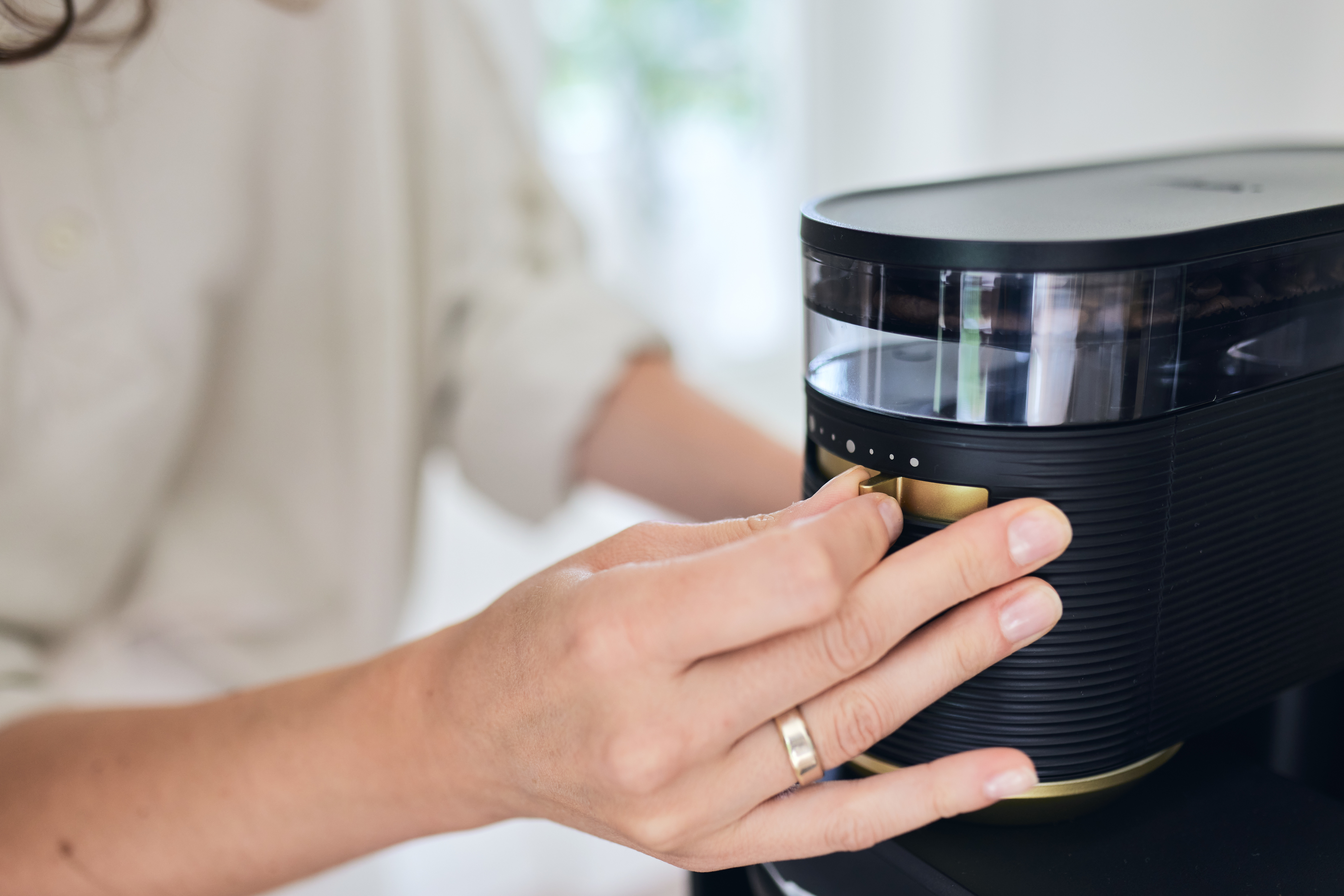 Osoba reguluje czarny ekspres do kawy. Widoczne złote detale. Białe tło.