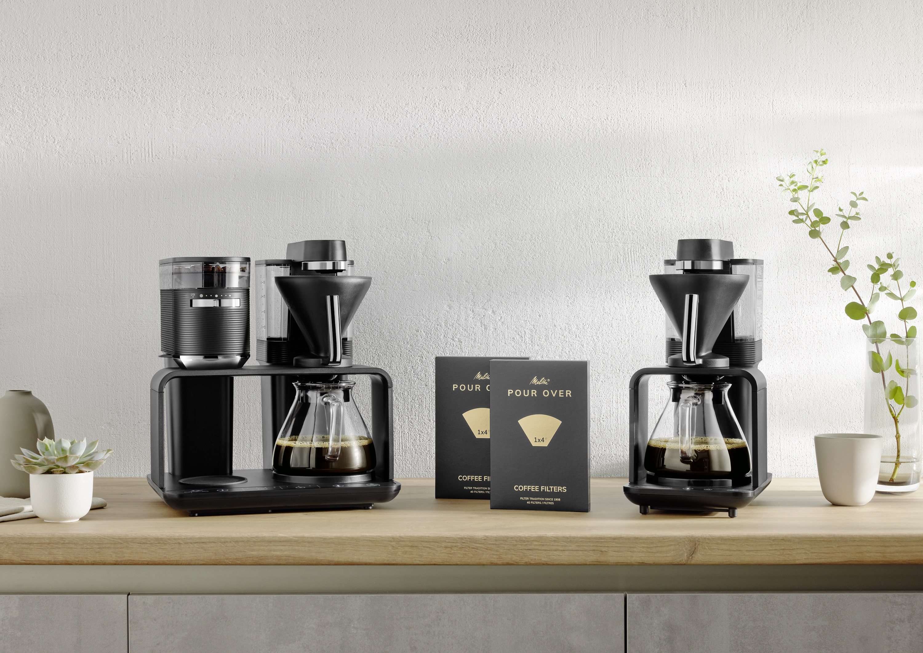 Kaffee-Setup mit Mahlwerk, Pour Over, Filtern und Kaffee in Glaskaraffe auf Holztisch.