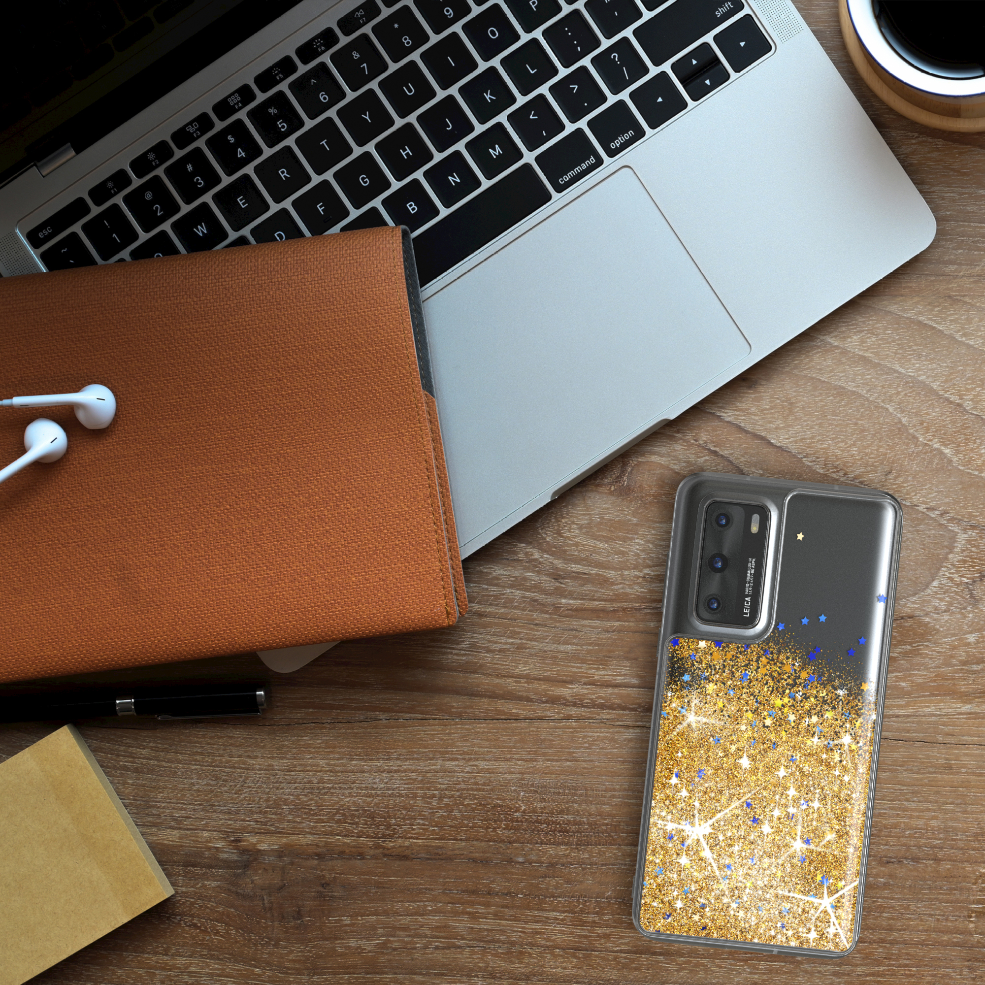 Eine Handyhülle auf einem Schreibtisch. Die Hülle hat ein Goldglitzer-Design mit blauen Sternen. Ein Laptop und ein Notizbuch sind ebenfalls vorhanden.