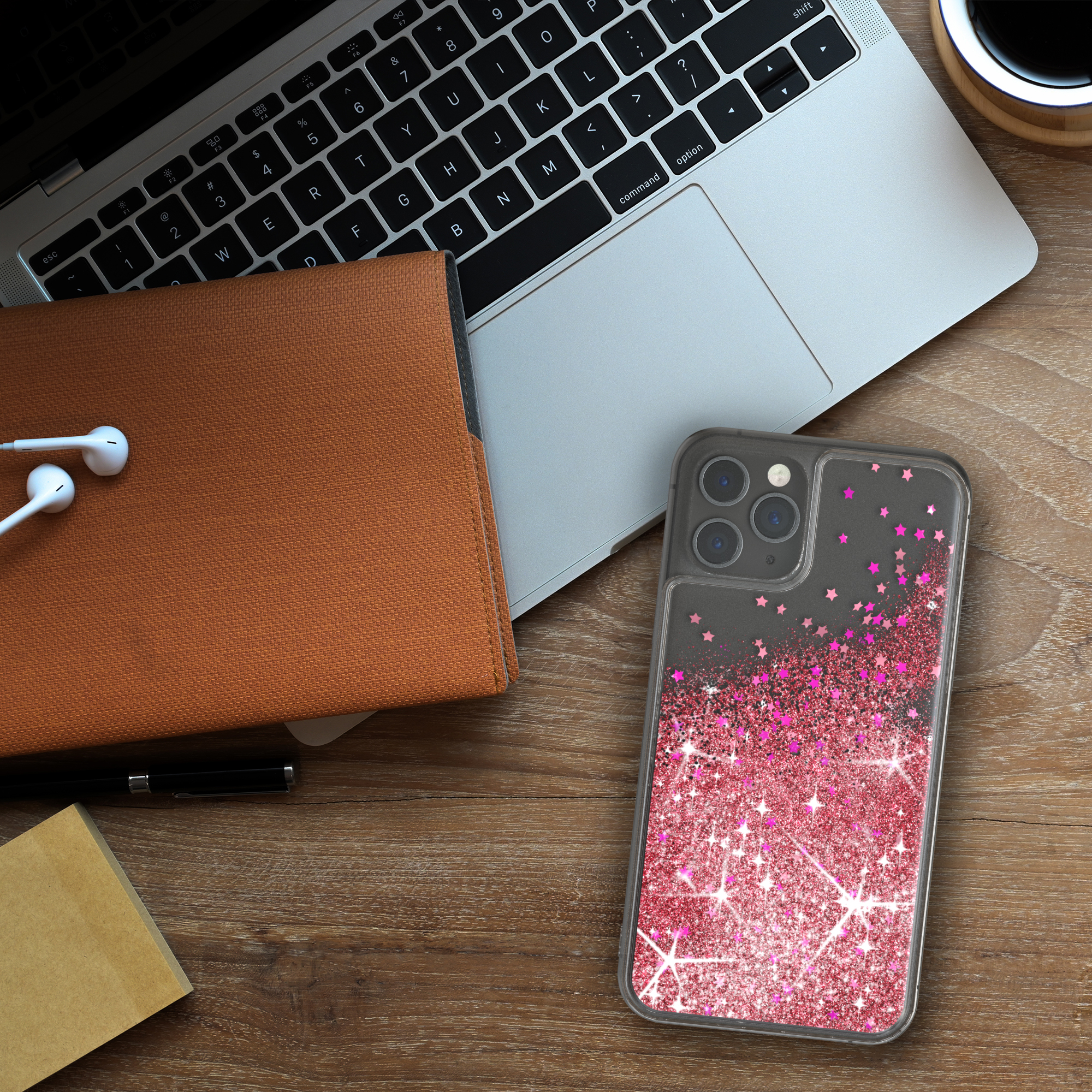 Telefon auf Holzschreibtisch mit Laptop, Notizbuch und Kopfhörern. Hülle mit Glitzer.