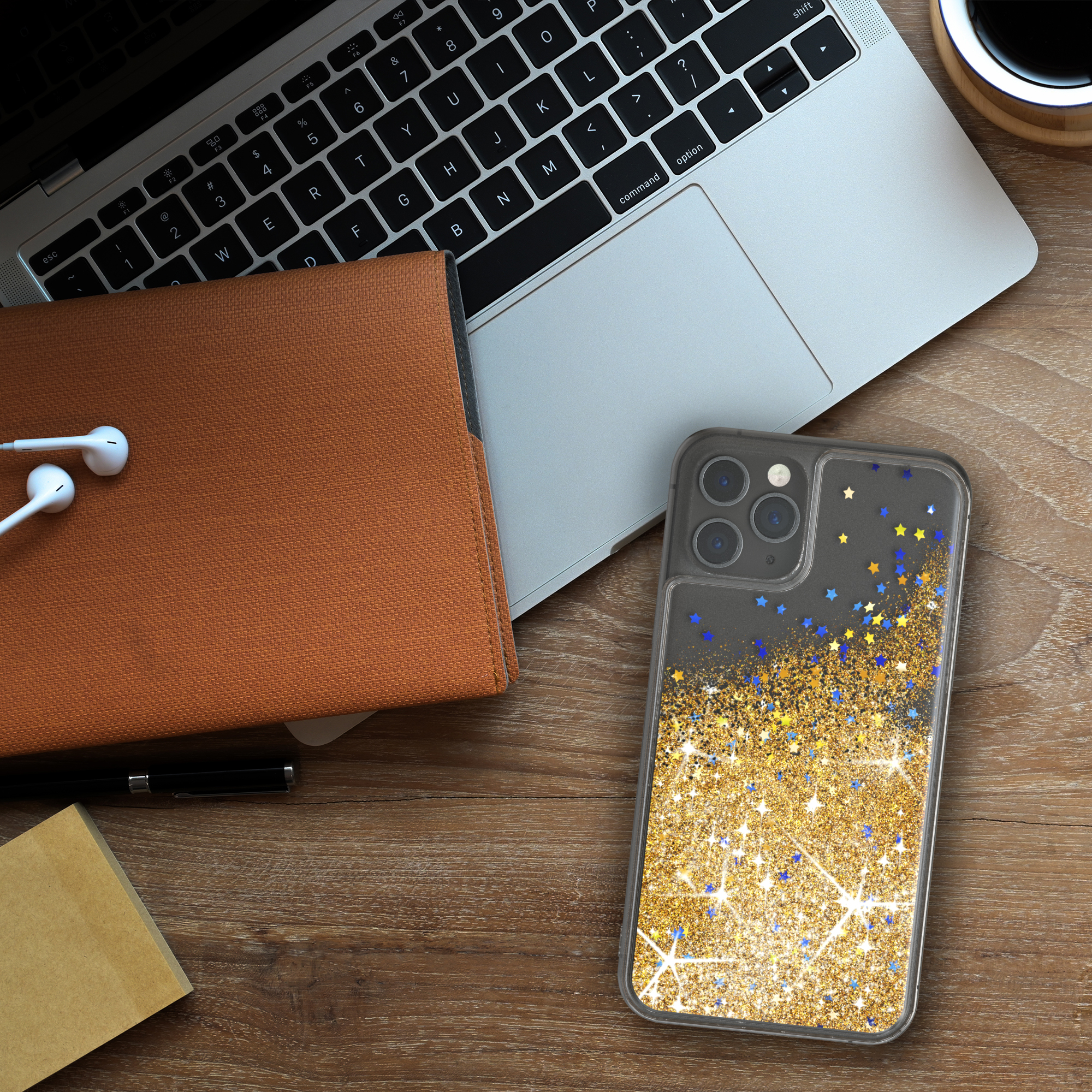 Eine Handyhülle mit goldenem Glitzerdesign liegt auf einem Holzschreibtisch mit Laptop und Notizblock.