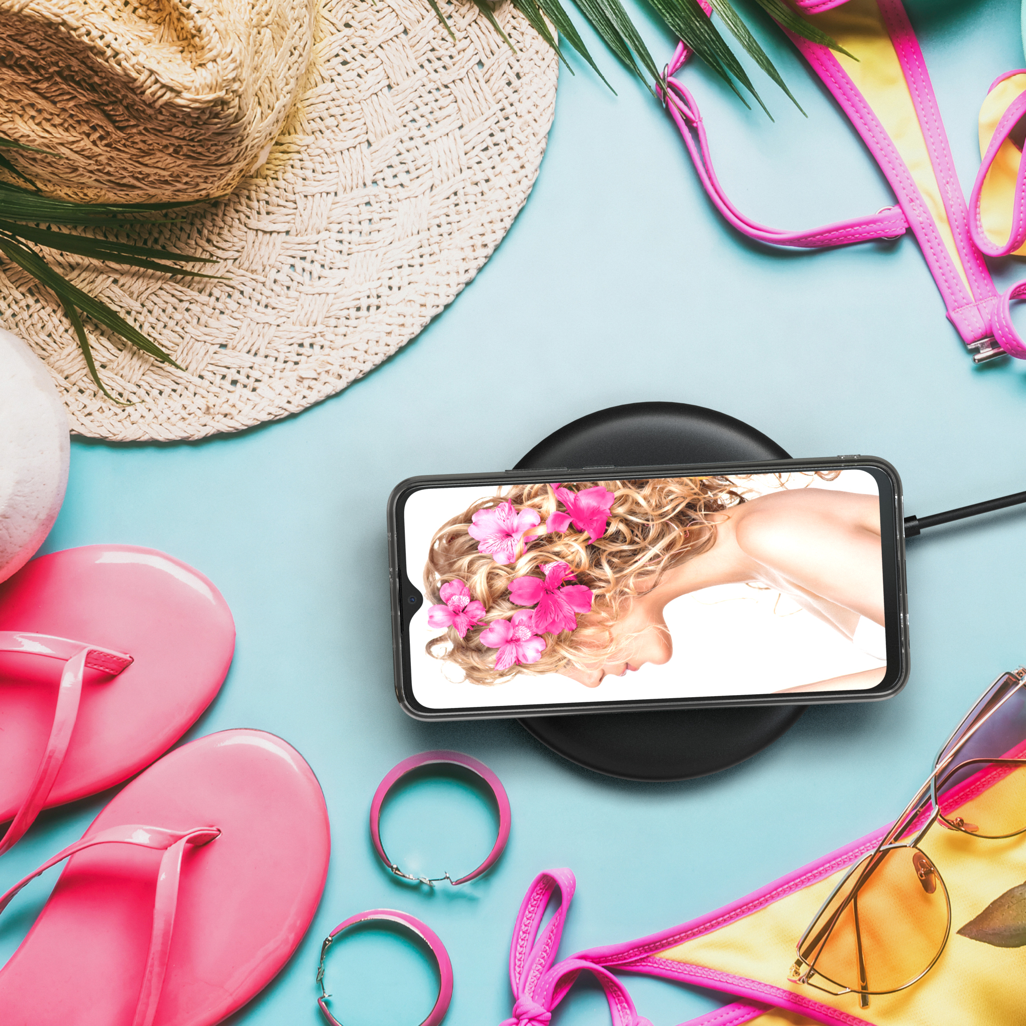Telefon auf kabellosem Ladegerät. Umgeben von Sommerartikeln. Frauenporträt auf dem Bildschirm.