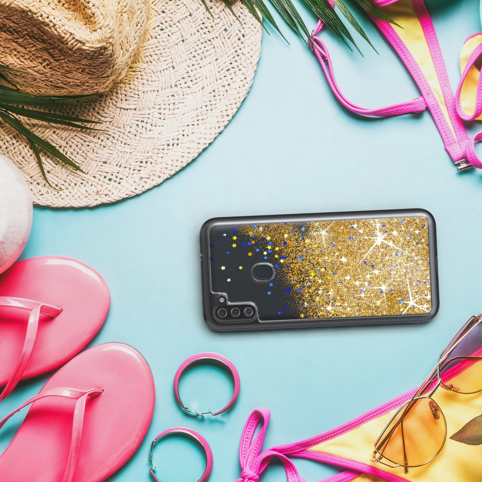 Handyhülle mit goldenem Glitzer und Sternen, umgeben von Strandaccessoires auf blauer Oberfläche.