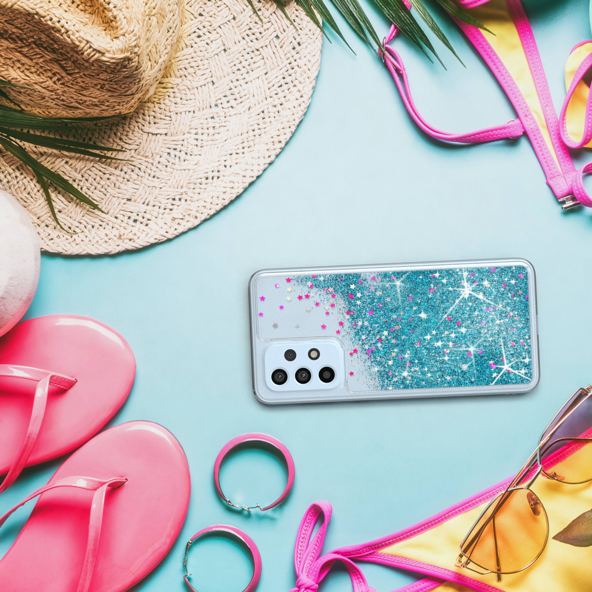 Handyhülle mit Glitzer und Sternen, auf blauem Hintergrund mit Accessoires: Hut, Flip-Flops, Sonnenbrille.