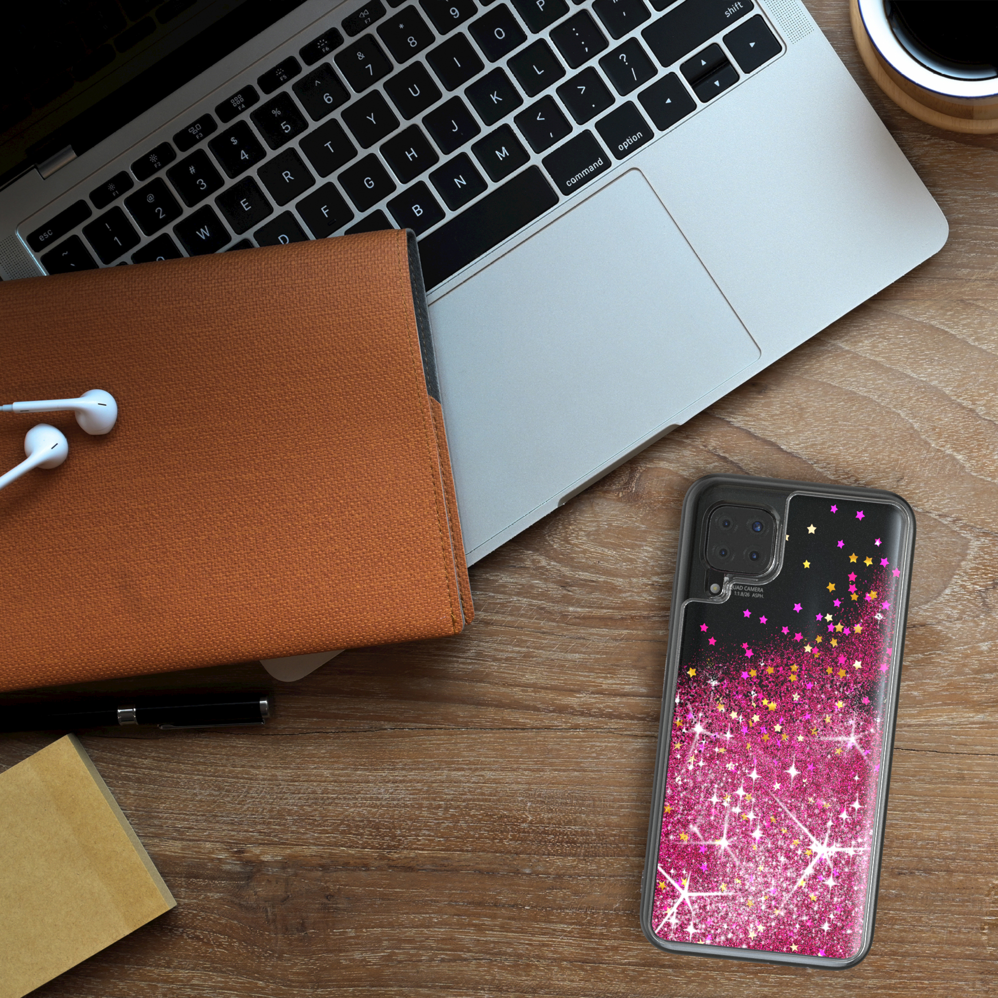 Telefon mit Glitzerhülle, Laptop, Notizblock, Kopfhörer und Stift auf Holz.