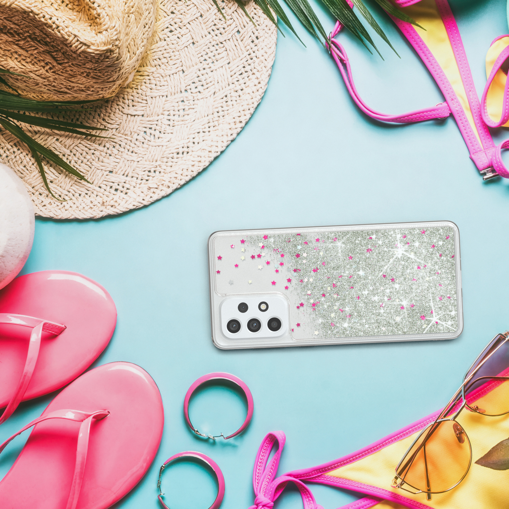 Telefon mit Glitzerhülle auf blauem Hintergrund mit Strandutensilien: Hut, Flip-Flops und Sonnenbrille.