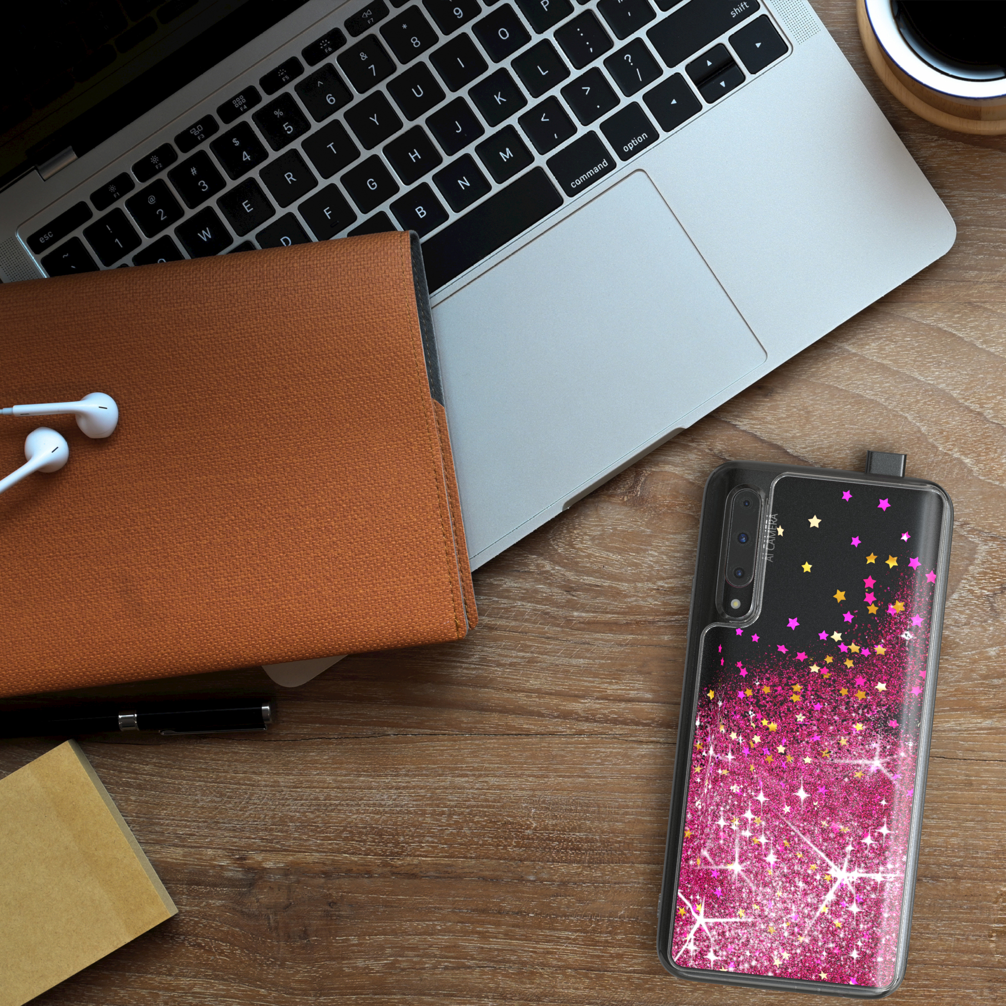 Ein Laptop, Notizbuch und Handyhülle auf einem Holztisch, mit einem rosa und goldenen Glitzerdesign.