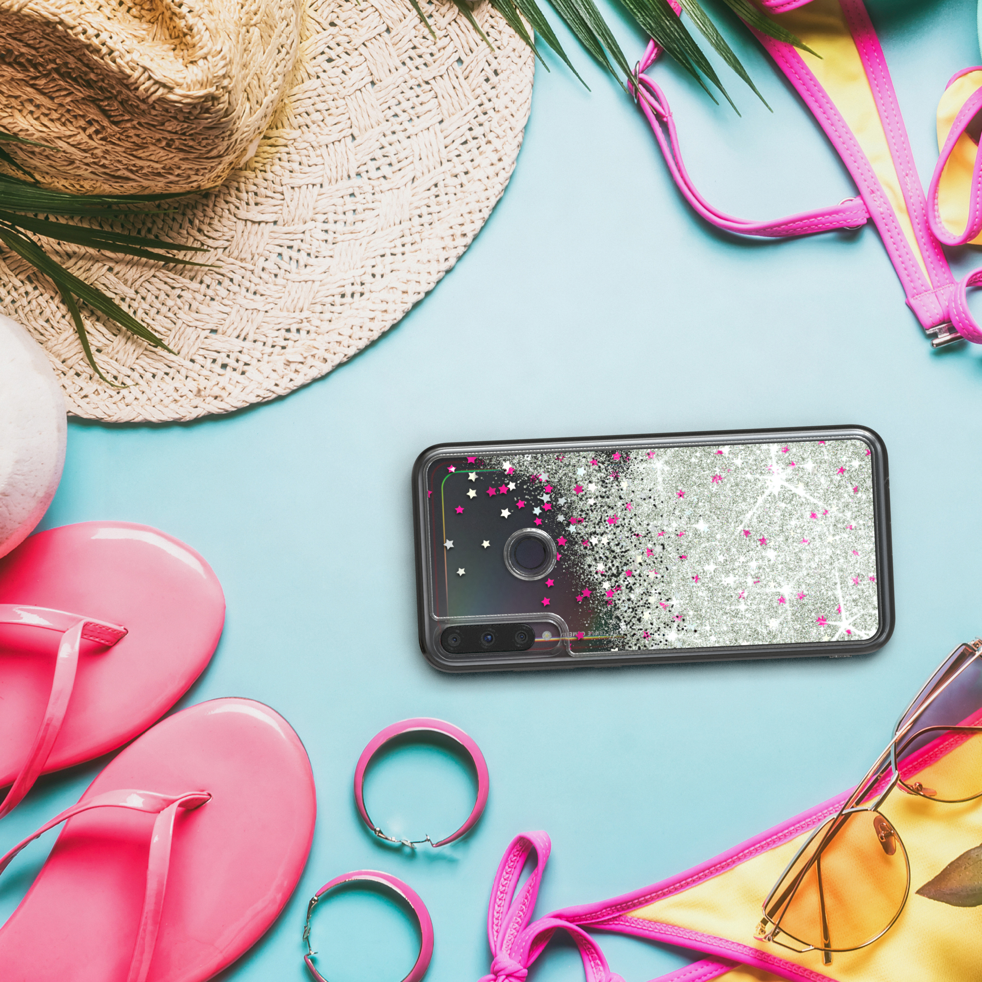 Telefon mit Glitzerhülle neben Strandutensilien. Hut, Sonnenbrille und Flip-Flops sichtbar.