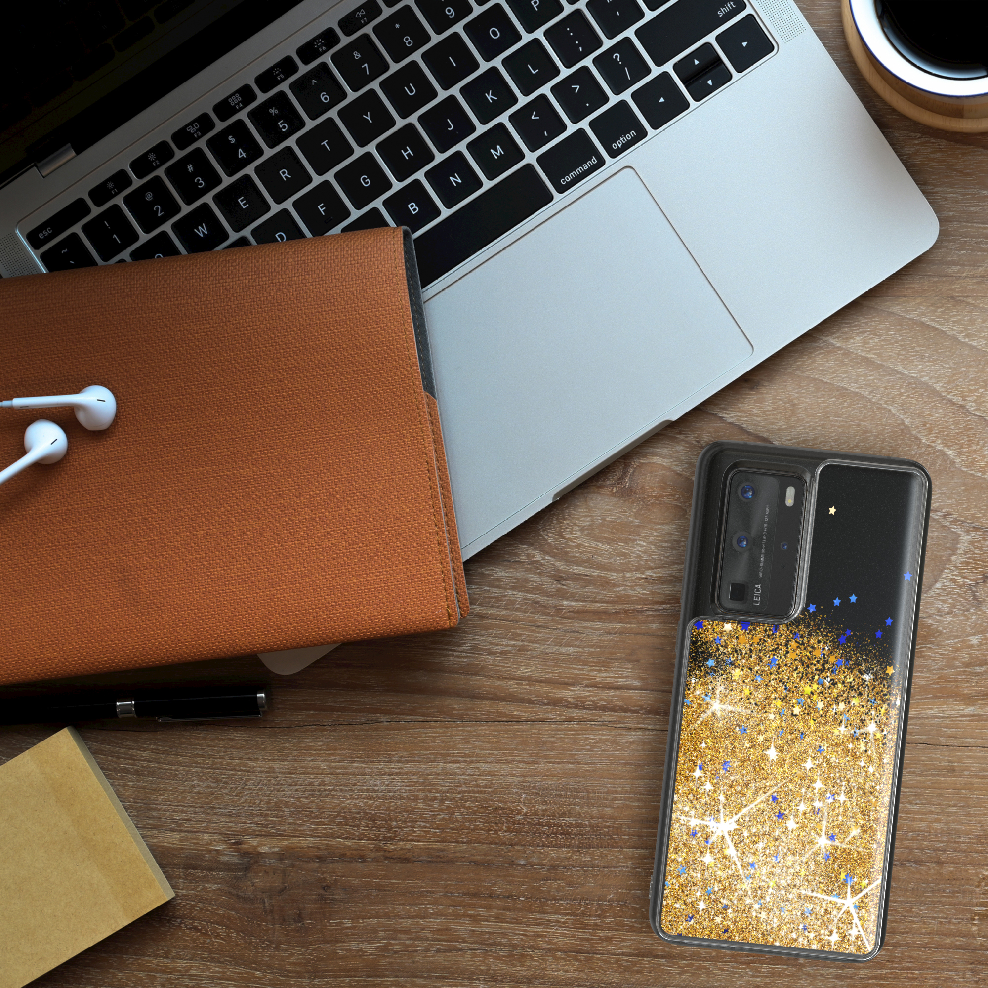 Laptop, Telefon mit Glitzerhülle, Notizbuch, Stift und Kopfhörer auf Holzschreibtisch.