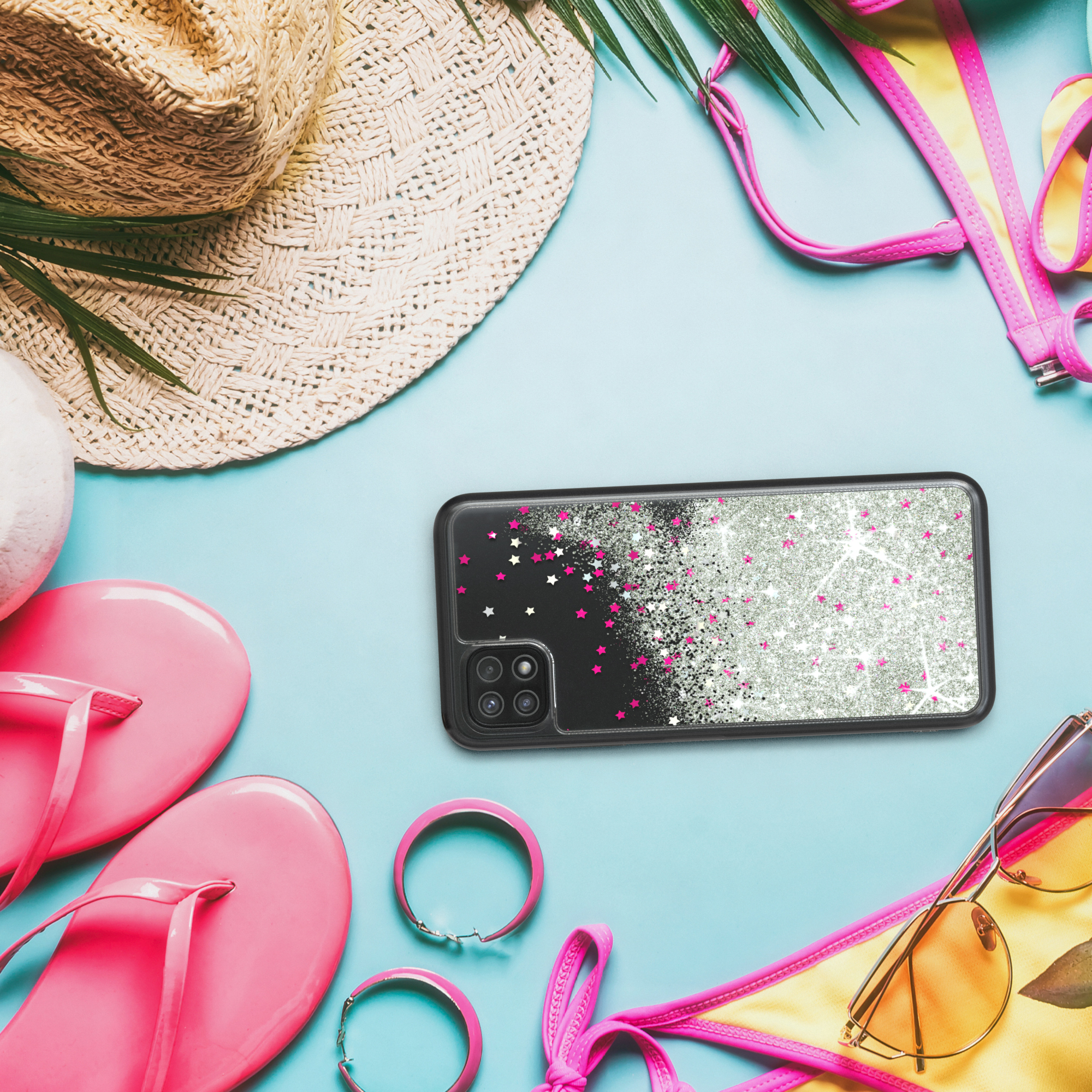 Ein Telefon in einer schwarzen Hülle mit Glitzer und Sternen liegt auf einer blauen Oberfläche mit Strandartikeln.