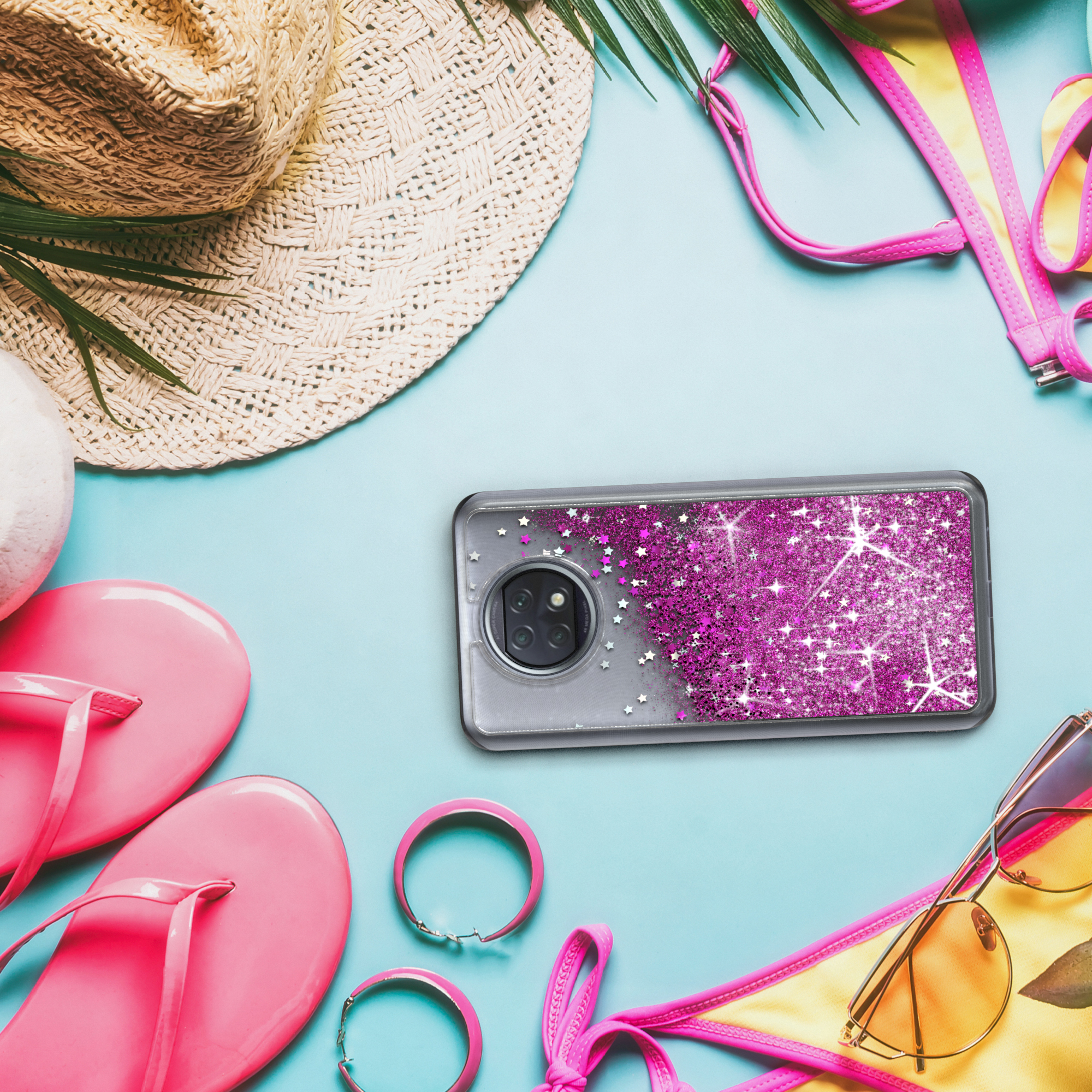 Handyhülle mit pinkfarbenem Glitzer auf einem Strand. Es gibt einen Strohhut, Sonnenbrille und Strandaccessoires.