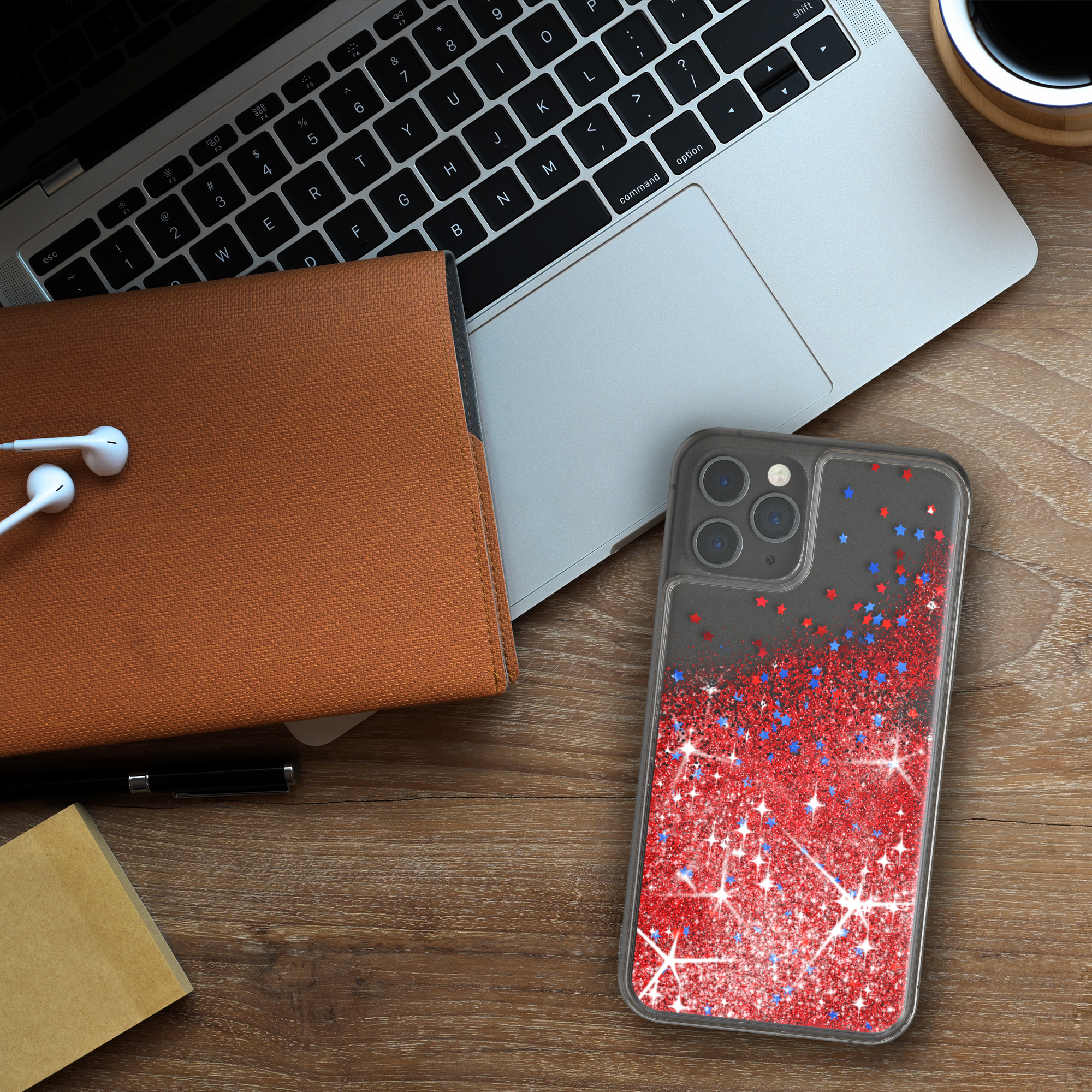 Handyhülle mit roten, blauen Glitzersternen auf einem Holzschreibtisch mit Laptop, Notizbuch und Kopfhörern.