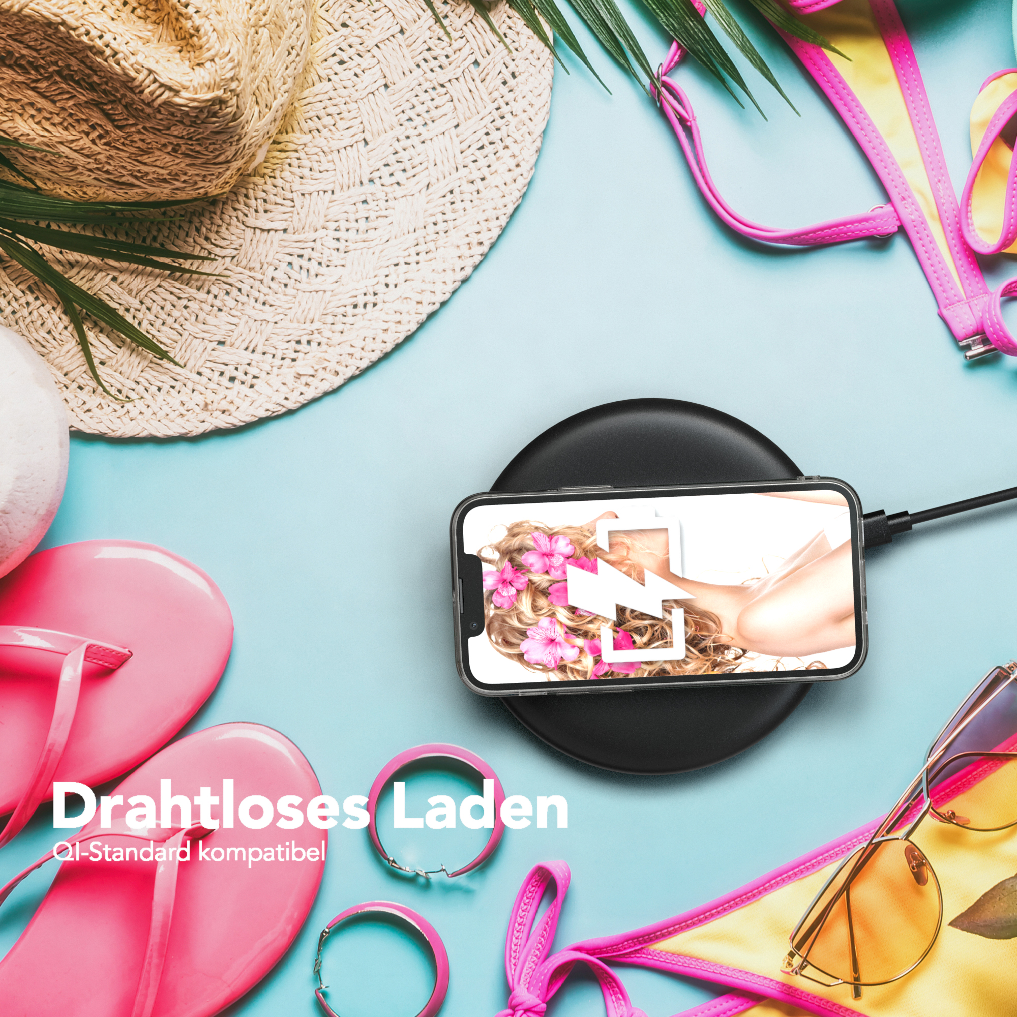 Ein Telefon wird drahtlos auf einem Pad geladen. Pinke Sandalen, Sonnenbrille und Strohhut sind dabei.