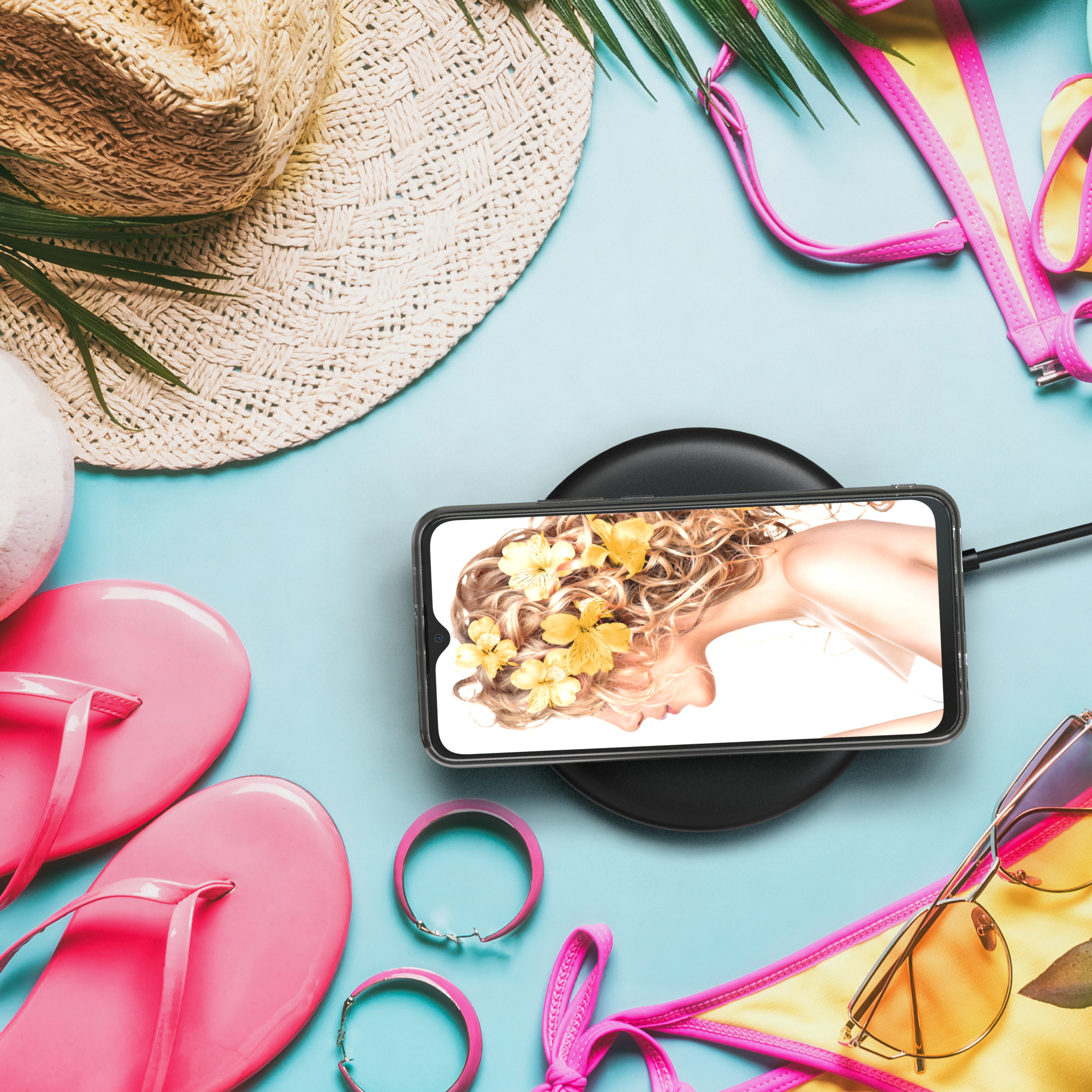 Ein Telefon mit klarer Hülle liegt auf einem kabellosen Ladegerät. Strandmotiv mit Sonnenbrille und Flip-Flops.