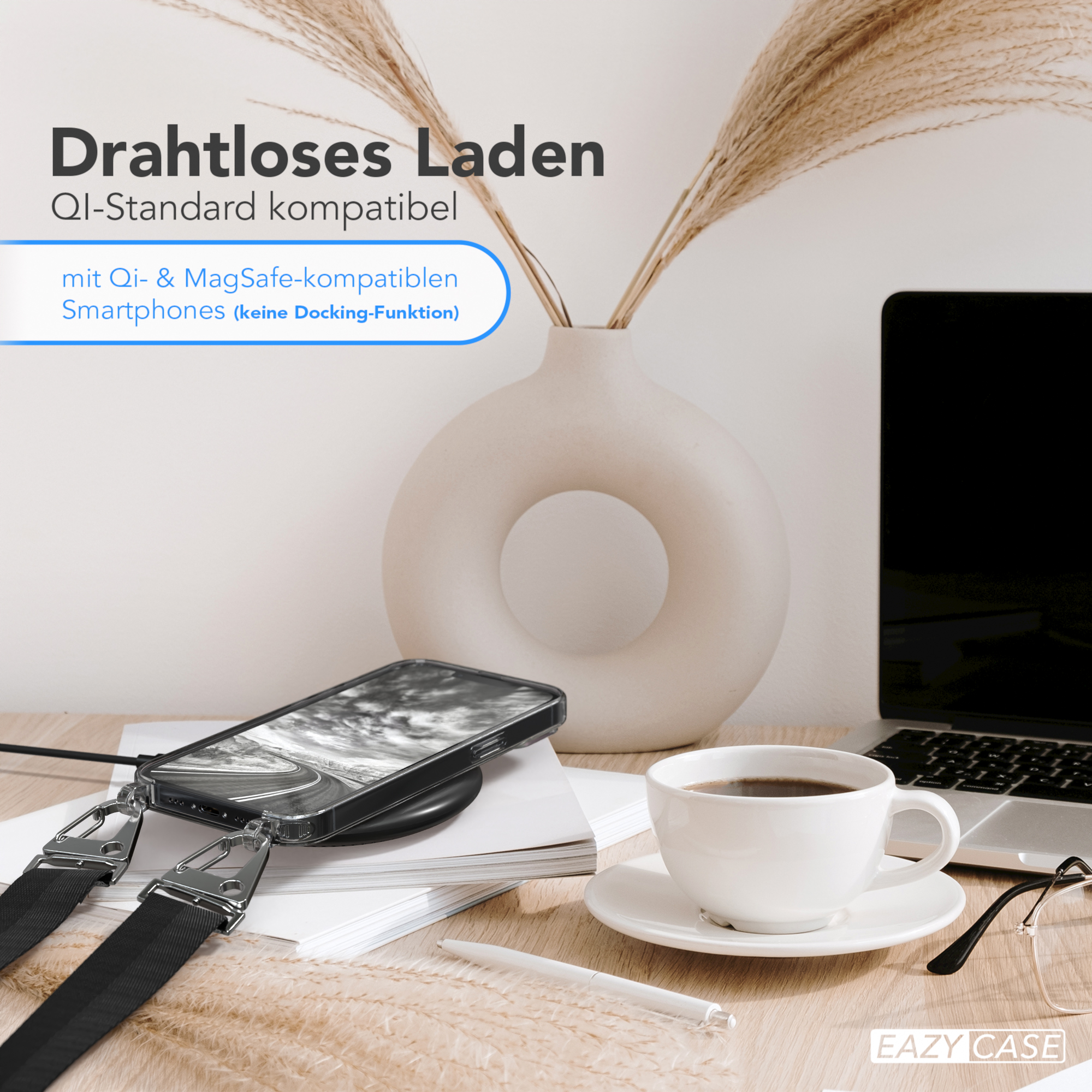 Ein Telefon auf einem kabellosen Ladegerät, eine Vase mit Pflanzen, ein Laptop und eine Tasse Kaffee auf einem Holztisch.