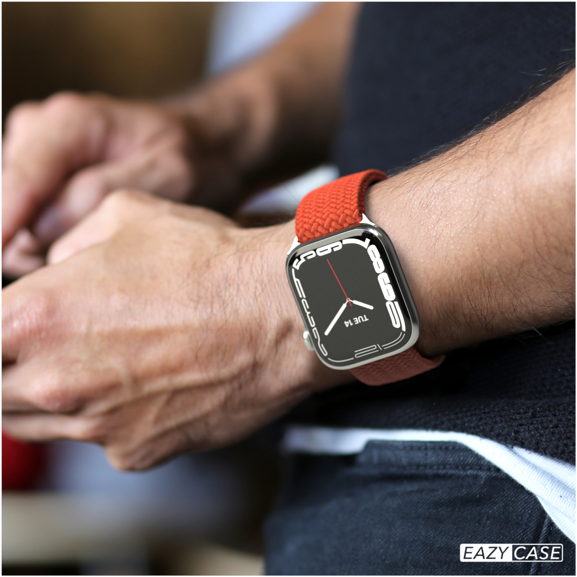Eine Person, die eine Apple Watch mit rotem Armband trägt. Die Uhr zeigt die Uhrzeit an.