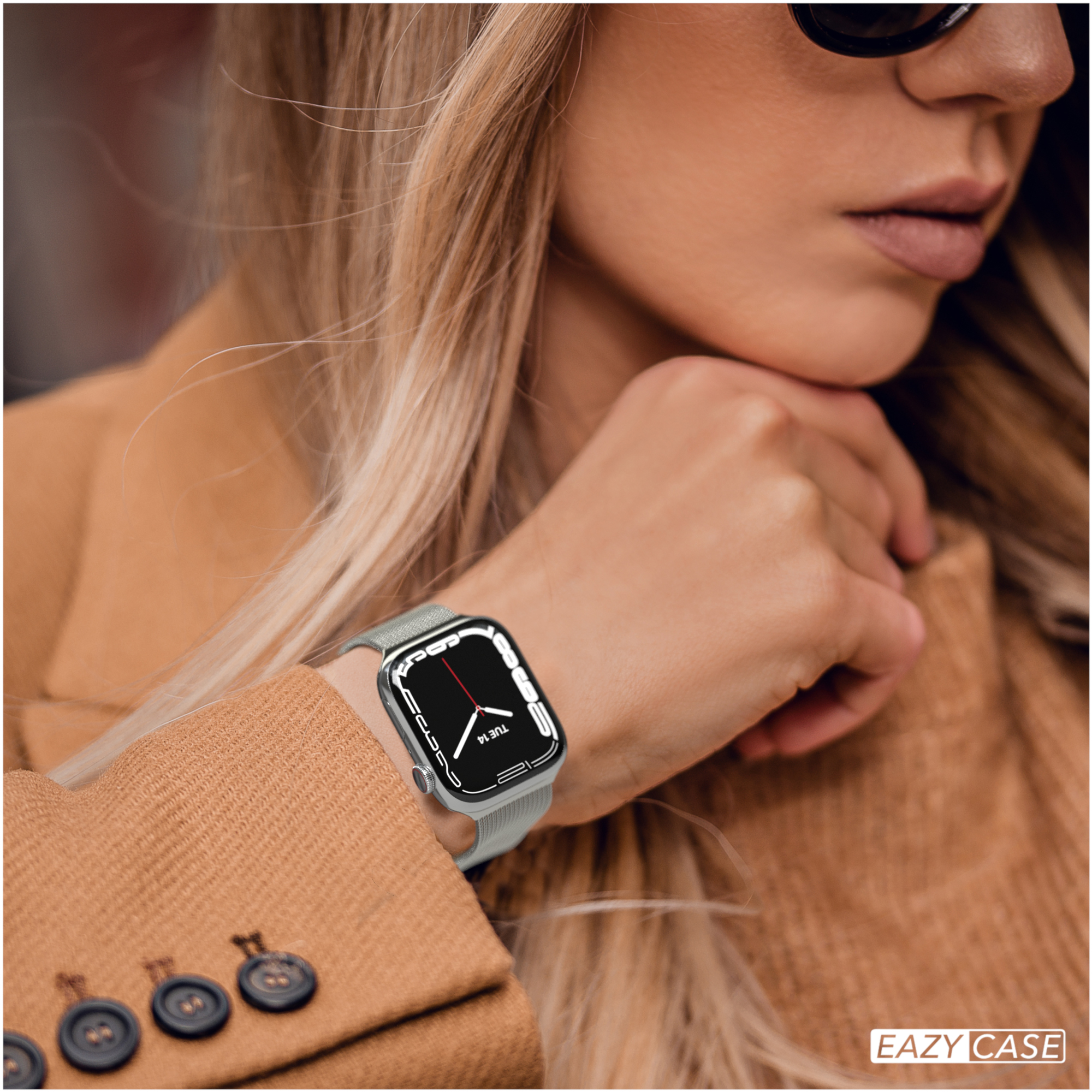 Frau mit Uhr. Die Uhr zeigt die Zeit. Sie trägt einen braunen Mantel.