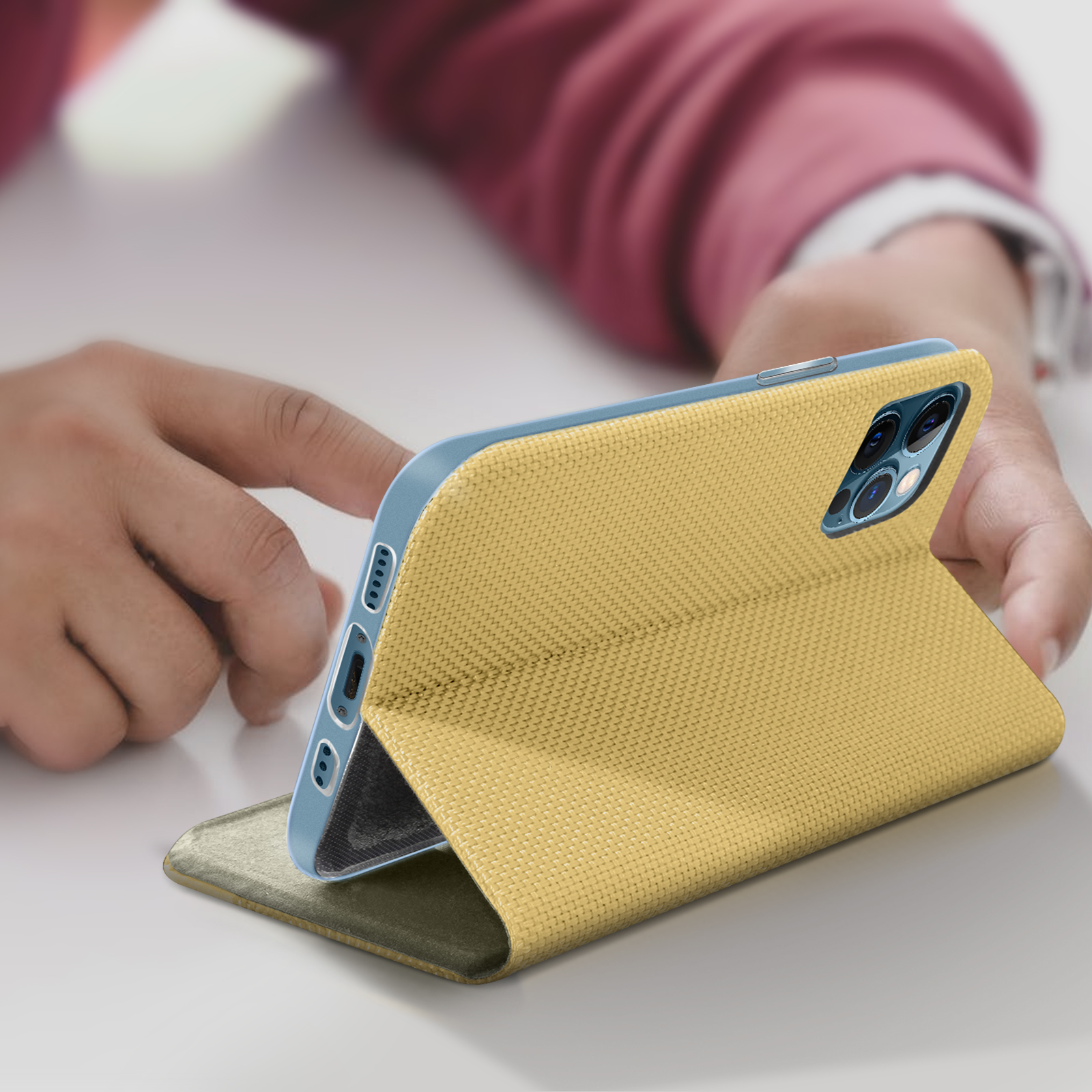 Eine Person hält eine gelbe Handyhülle. Das Telefon liegt auf einem Tisch. Die Hülle hat einen Ständer.
