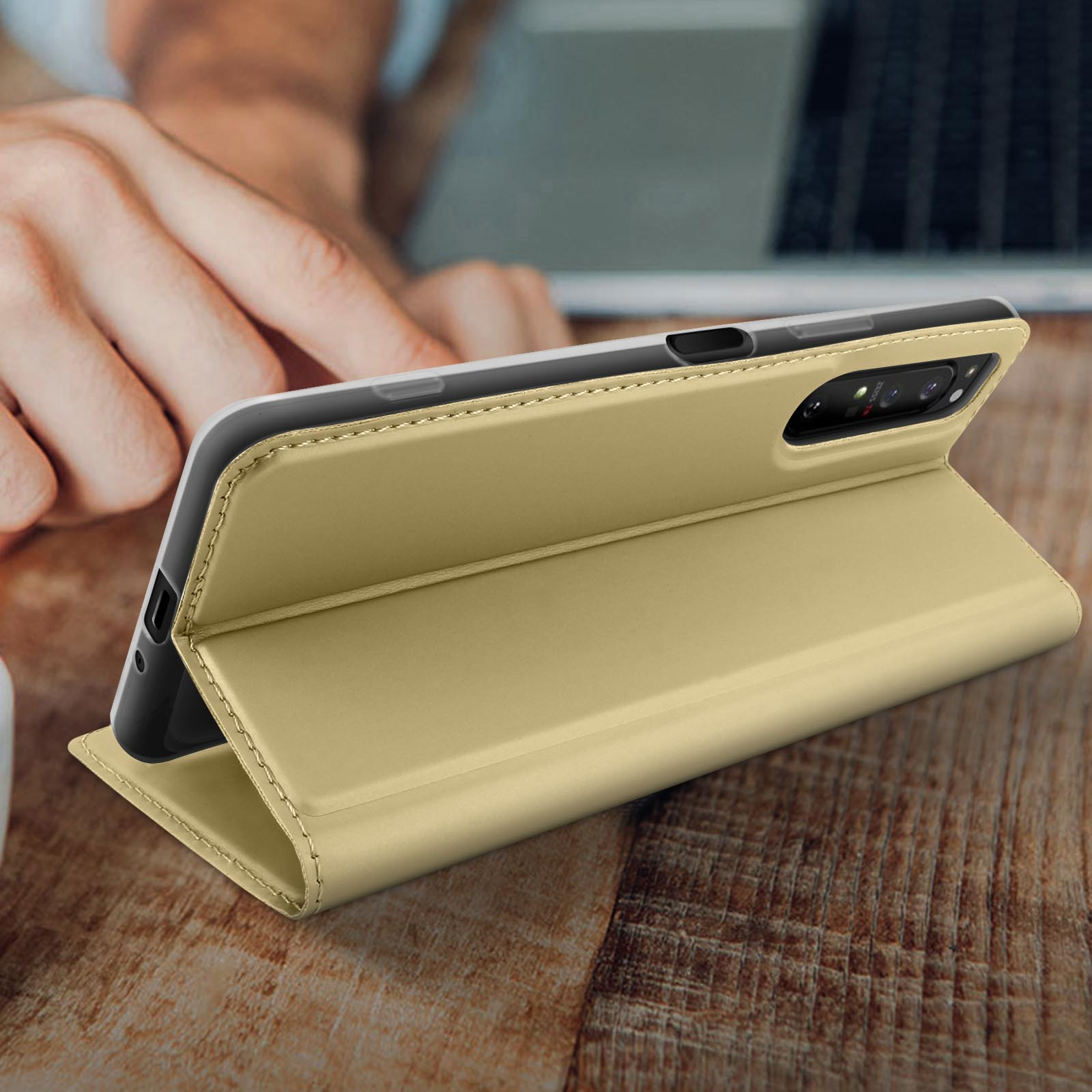 Geöffnete goldene Handyhülle auf einem Holztisch. Schwarzes Telefon innen. Hand hält Telefon.