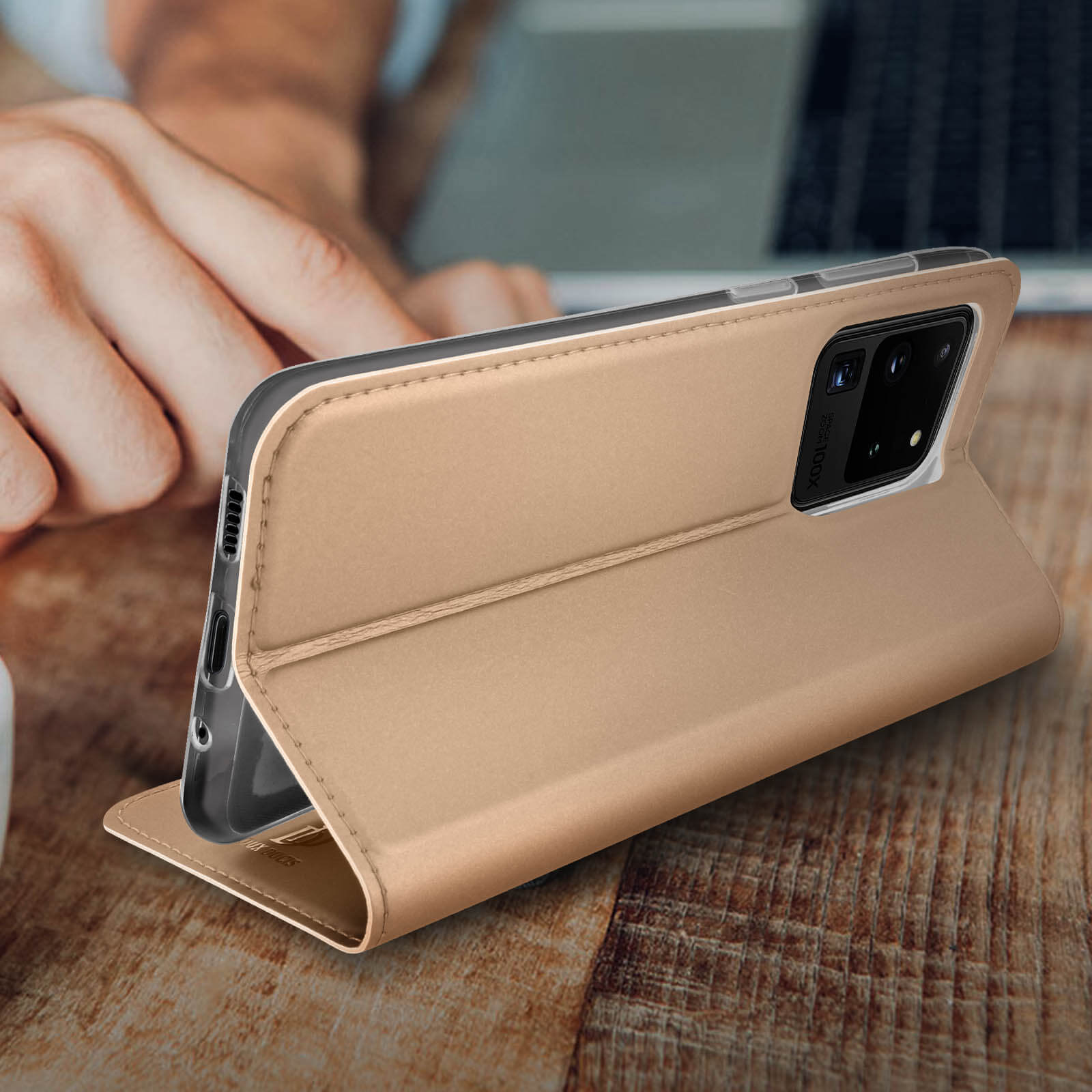 Eine goldene Handyhülle geöffnet, ein Telefon auf Holzoberfläche abstützend. Die Kamera ist sichtbar.