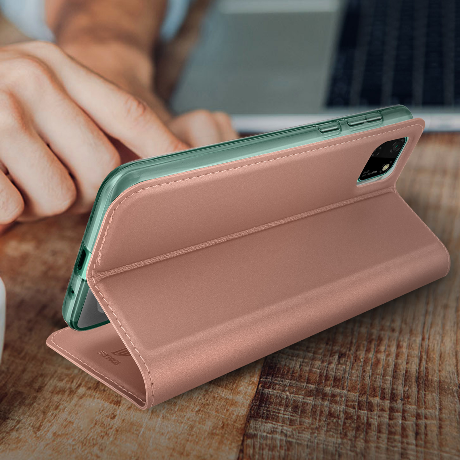 Custodia per telefono rosa, aperta, con telefono dentro, su un tavolo di legno con mano.
