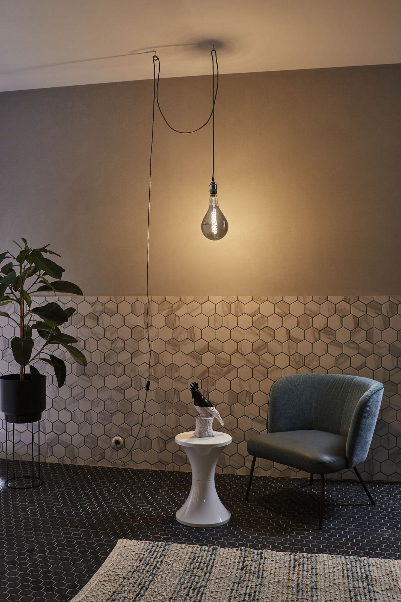 Ein stilvolles Interieur mit einer hängenden Glühbirne, einer Pflanze, einem Hocker, einem Stuhl und einer gemusterten Wand.