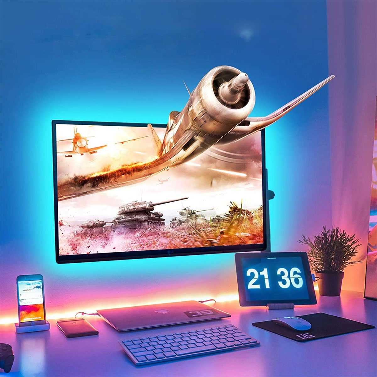 Configuración de juego con monitor mostrando avión, escritorio con tableta, teclado, teléfono y luces.