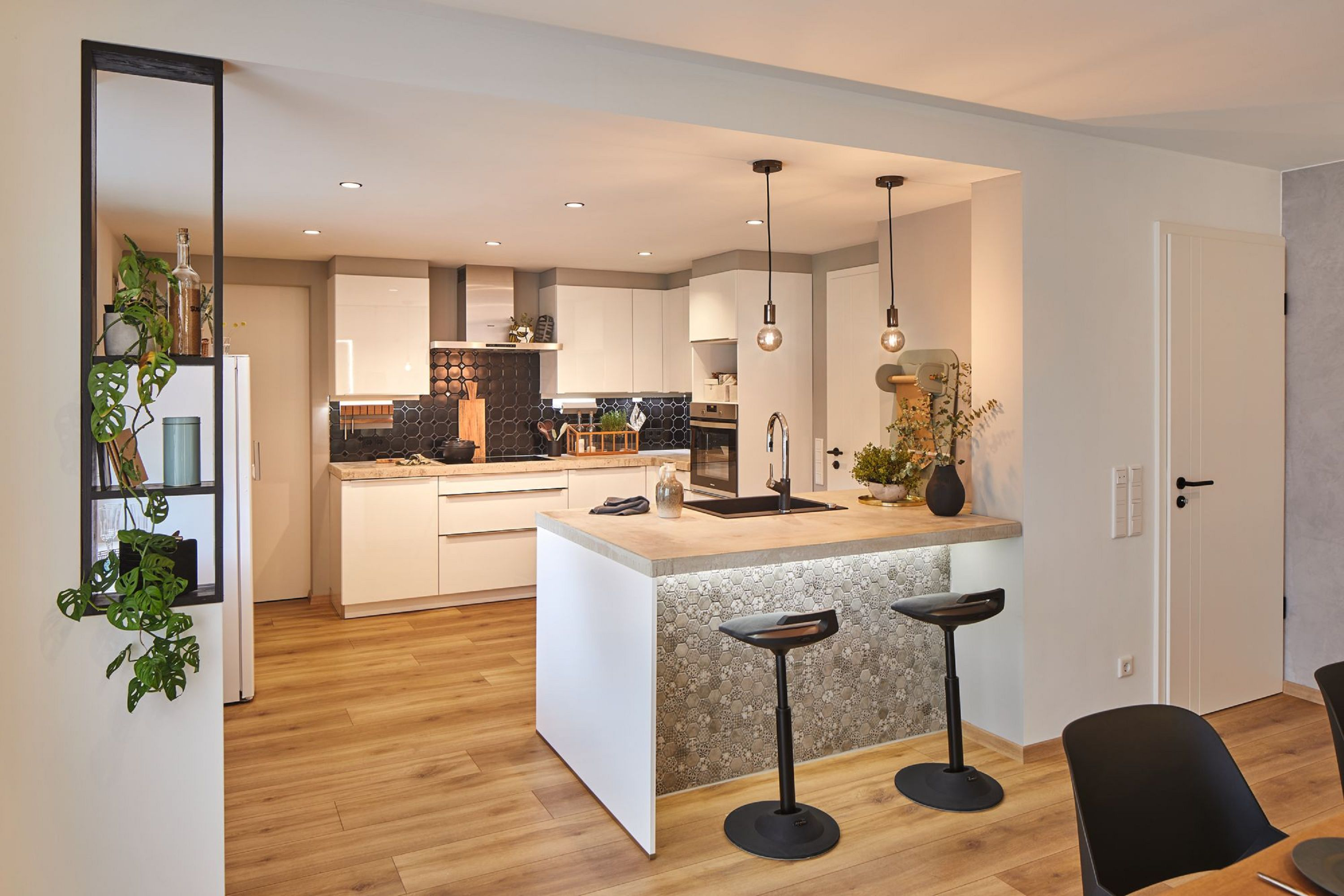 Nowoczesna kuchnia z białymi szafkami, drewnianą podłogą, czarną wyspą z lampami wiszącymi.