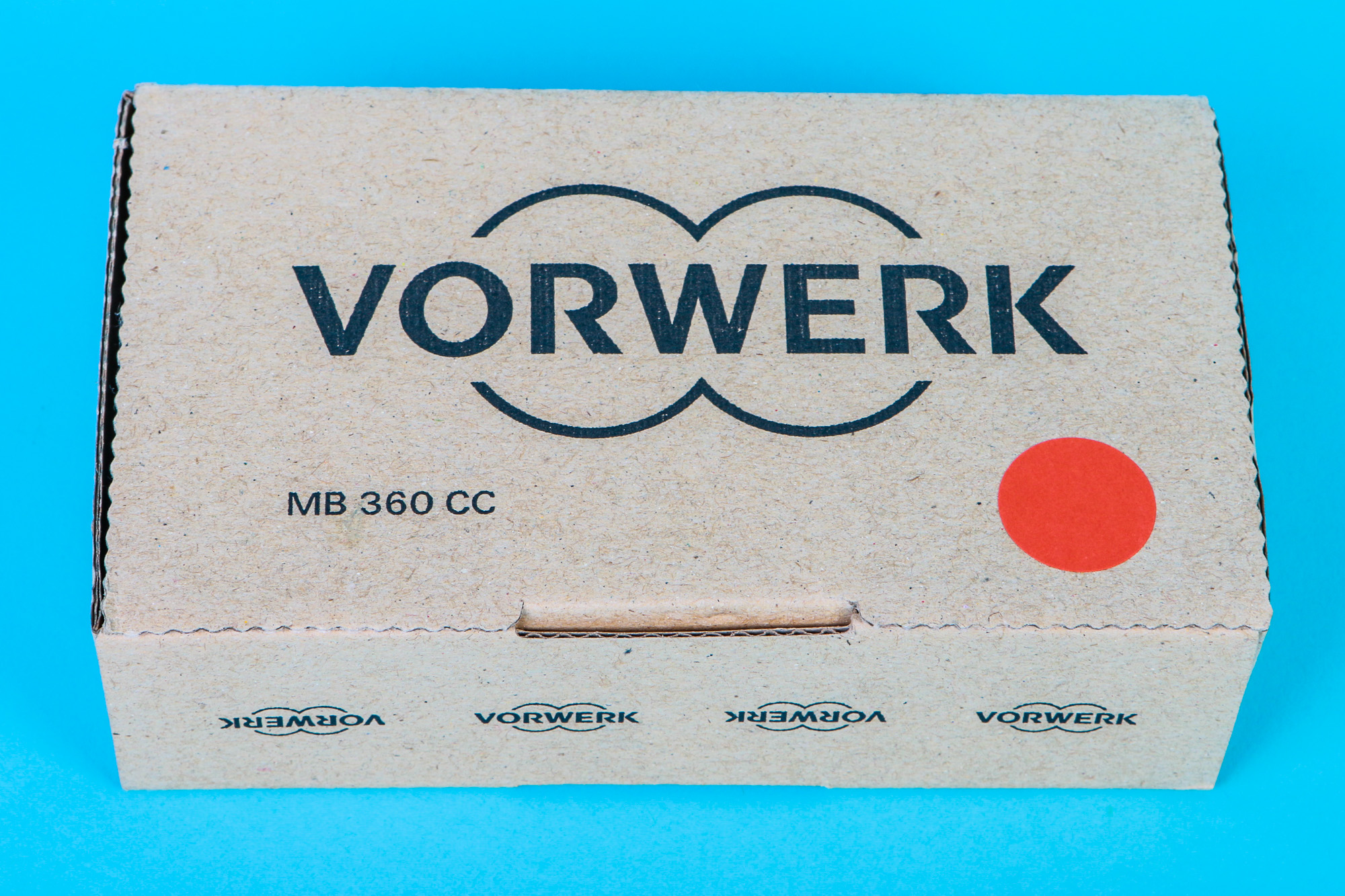 Ein Pappkarton mit dem Wort VORWERK und einem roten Kreis auf einer blauen Oberfläche.