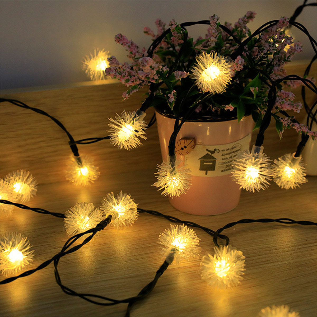 Ein Tisch mit kleinen, leuchtenden, weißen, kugelförmigen Lichtern und rosa Blumen in einem Topf.