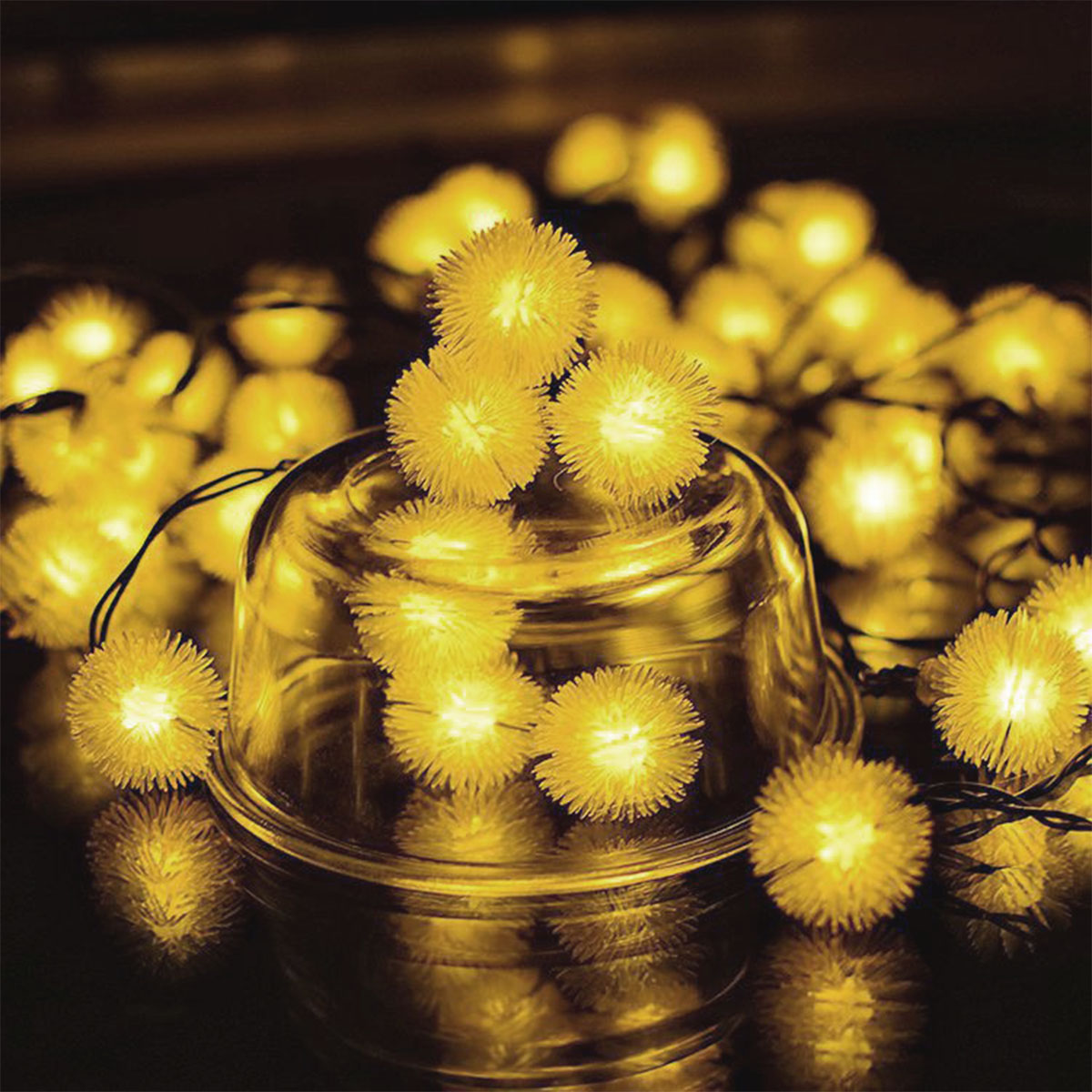 Nahaufnahme von gelben dekorativen Lichtern in einer Glasschale auf dunkler, reflektierender Oberfläche.