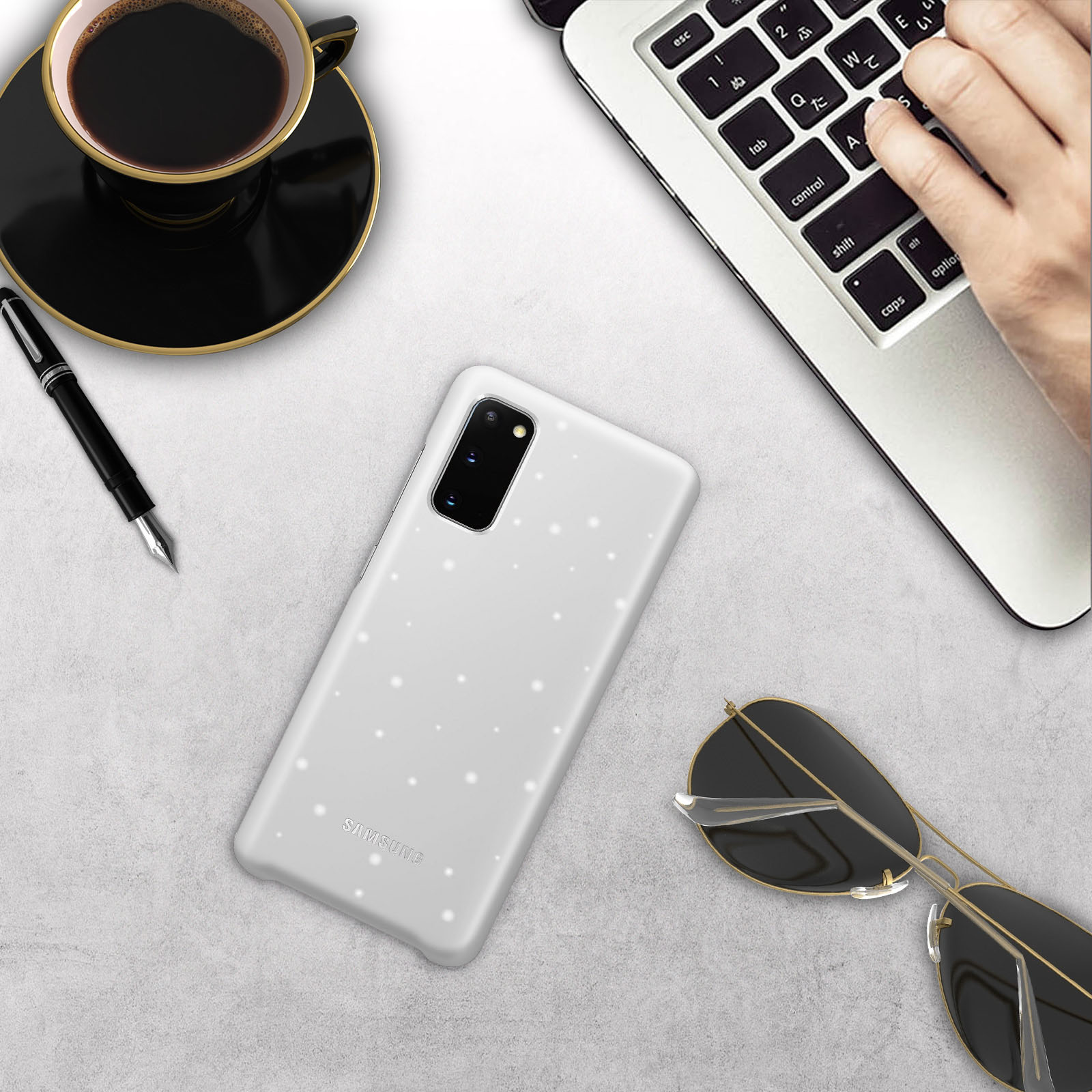 Una custodia bianca per telefono con puntini bianchi, una penna, occhiali da sole e una tazza di caffè su una scrivania.