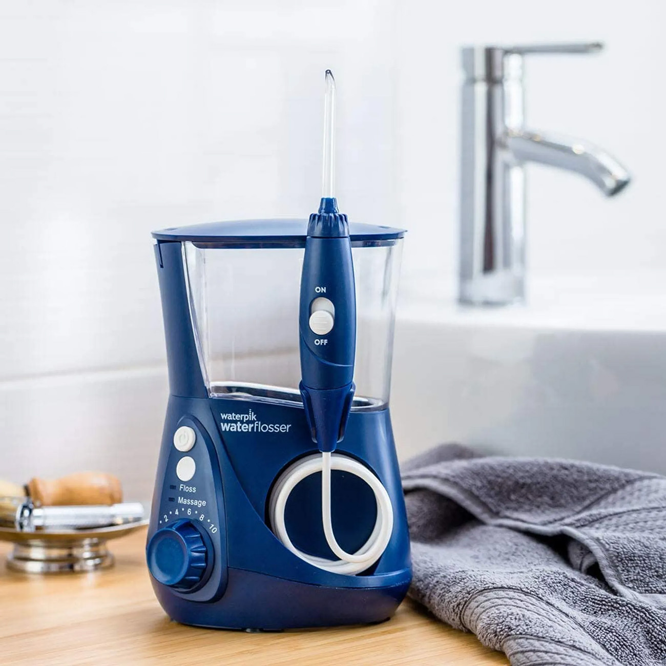 Blauer Waterpik-Wasserfloßer auf einer Holztheke. Waschbecken und Wasserhahn im Hintergrund.