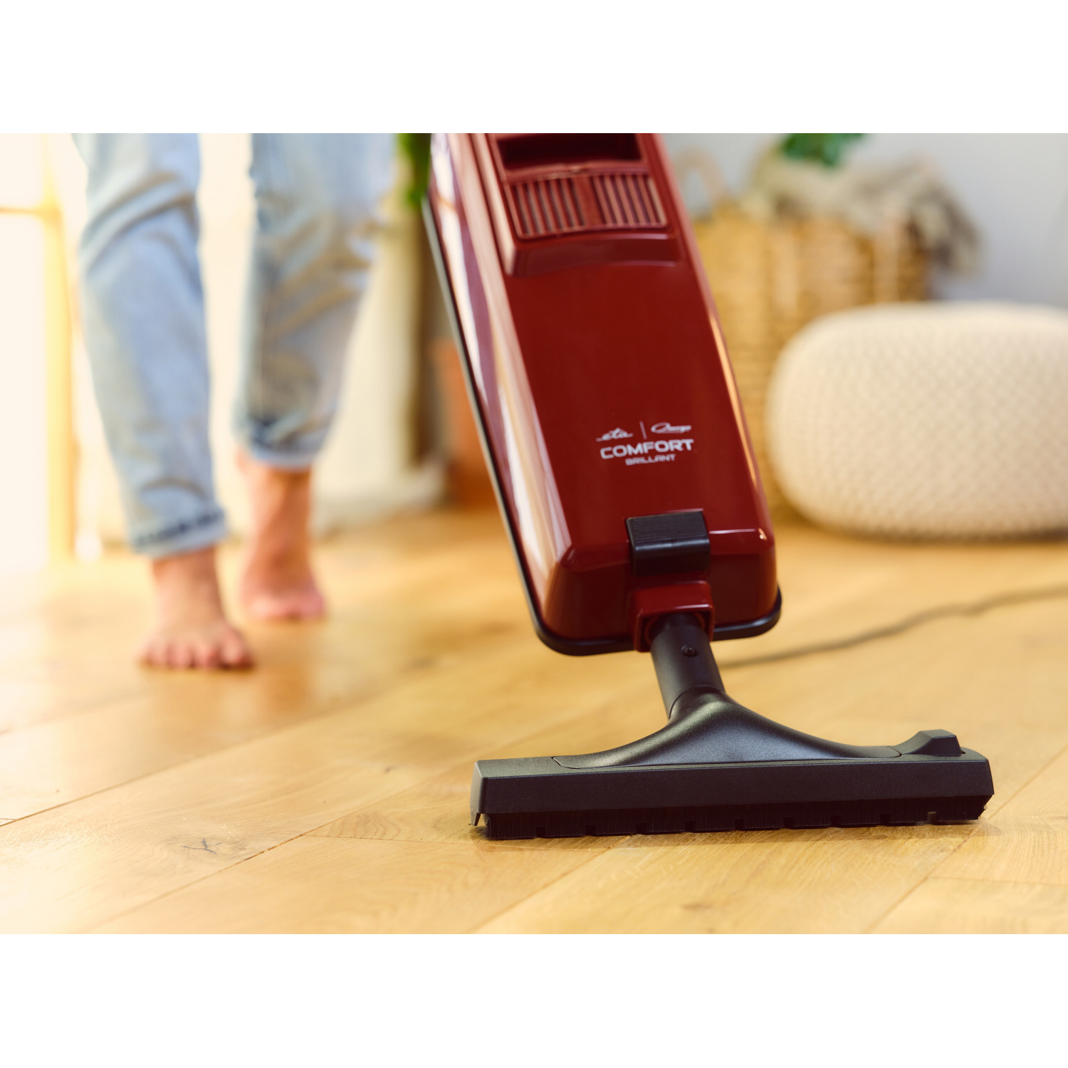Die Füße und Beine einer Person und ein roter Staubsauger auf dem Holzboden.