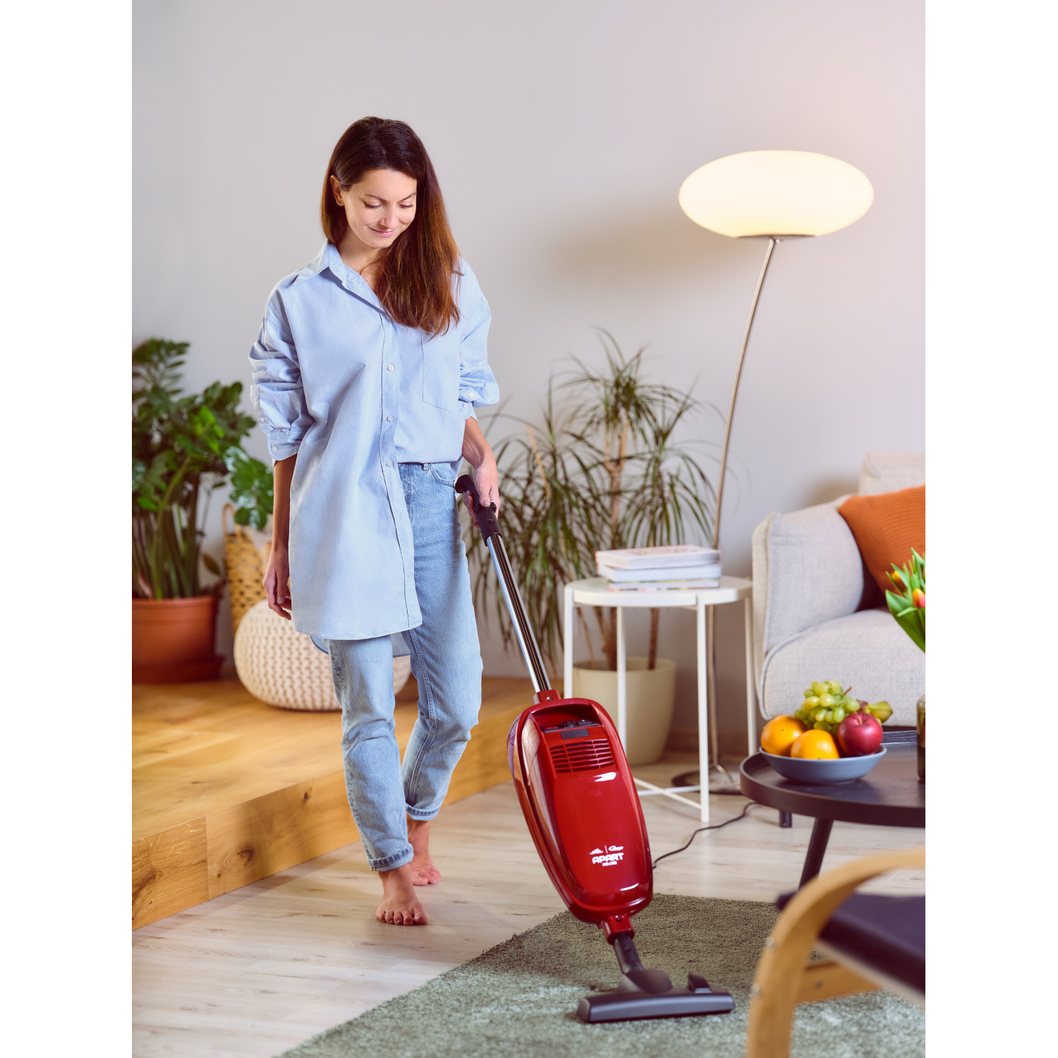 Frau saugt Wohnzimmer. Roter Staubsauger und Holzboden.