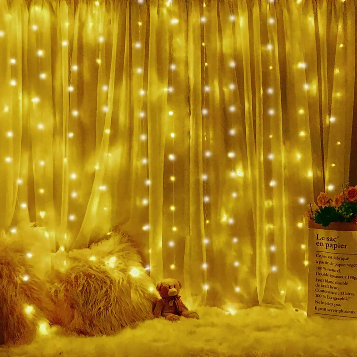 Goldene Lichter auf einem gelben Vorhang und Boden, mit einem Teddybär und einer Papiertüte.