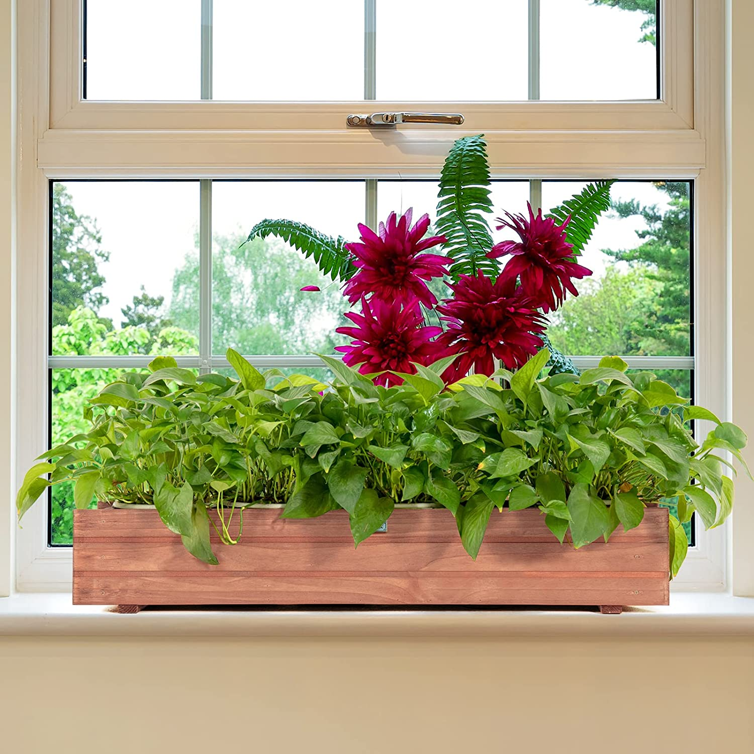 Ein hölzerner Pflanzkasten steht auf einer Fensterbank mit Blumen. Grüne Pflanzen und rote Blumen sind sichtbar.