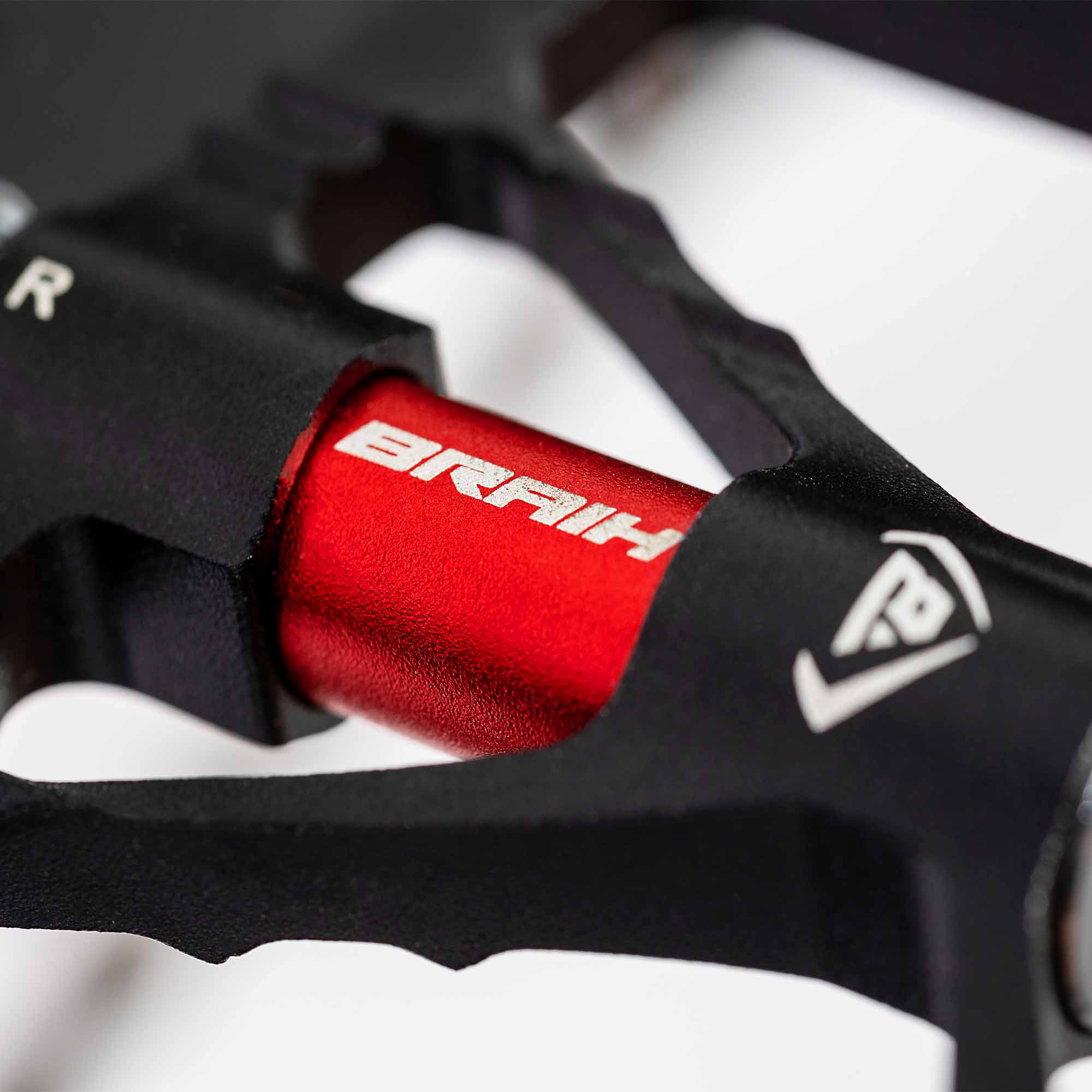 Primer plano de un pedal de bicicleta rojo y negro con la marca BRAIH visible.