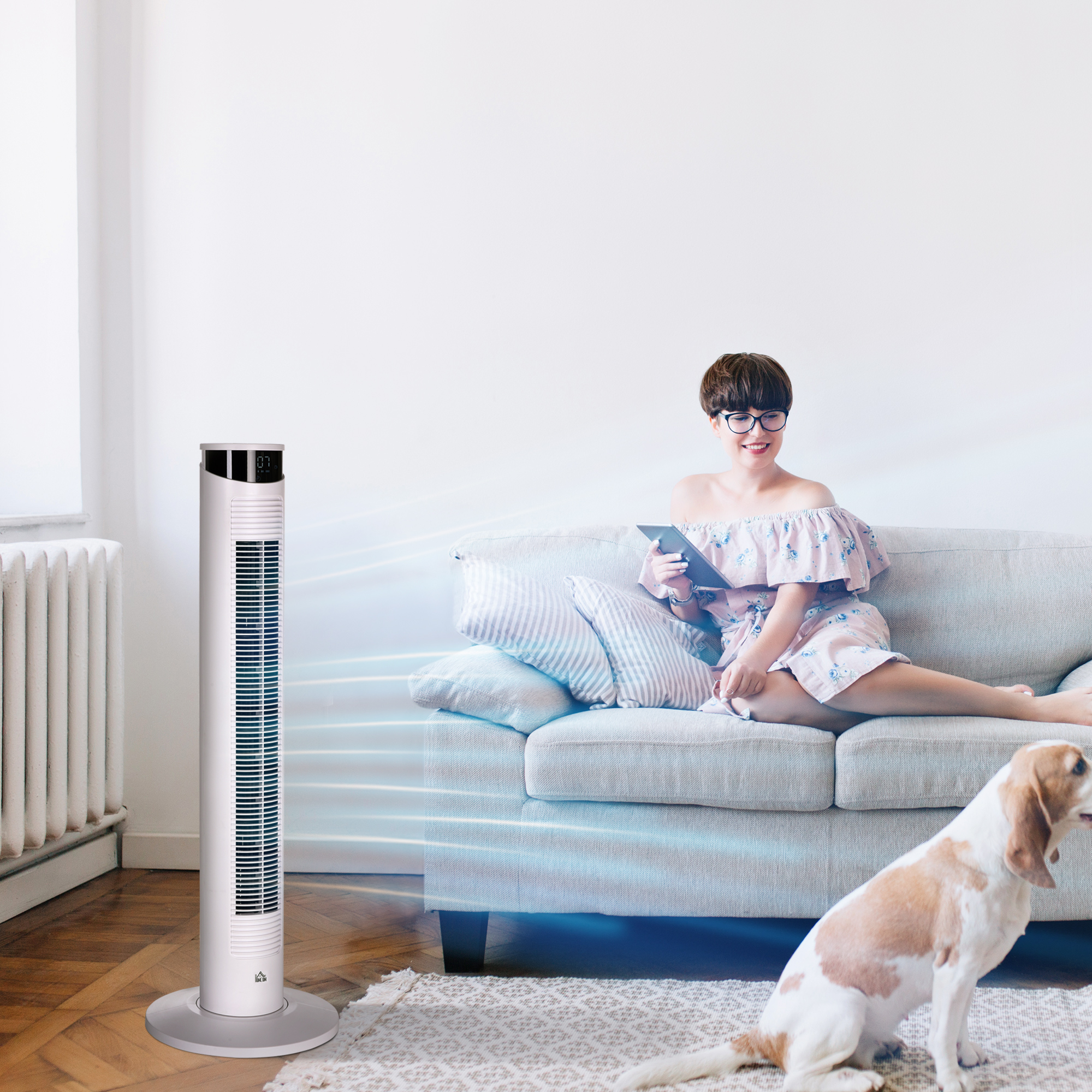 Mujer en un sofá usando una tableta, con un ventilador de pie y un perro en la habitación.