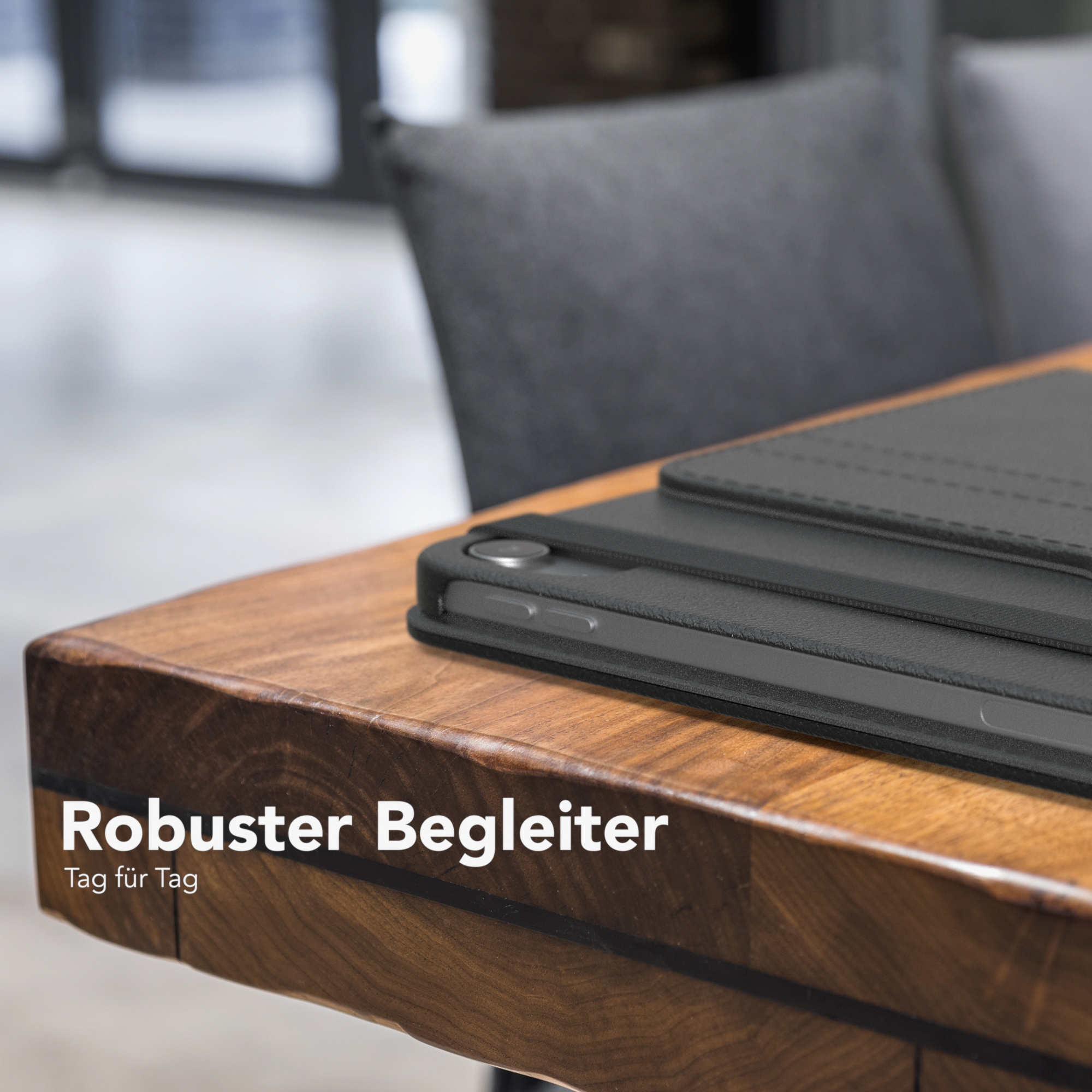 Eine schwarze Tablet-Hülle auf einem Holztisch, ein dunkler Stuhl im Hintergrund.