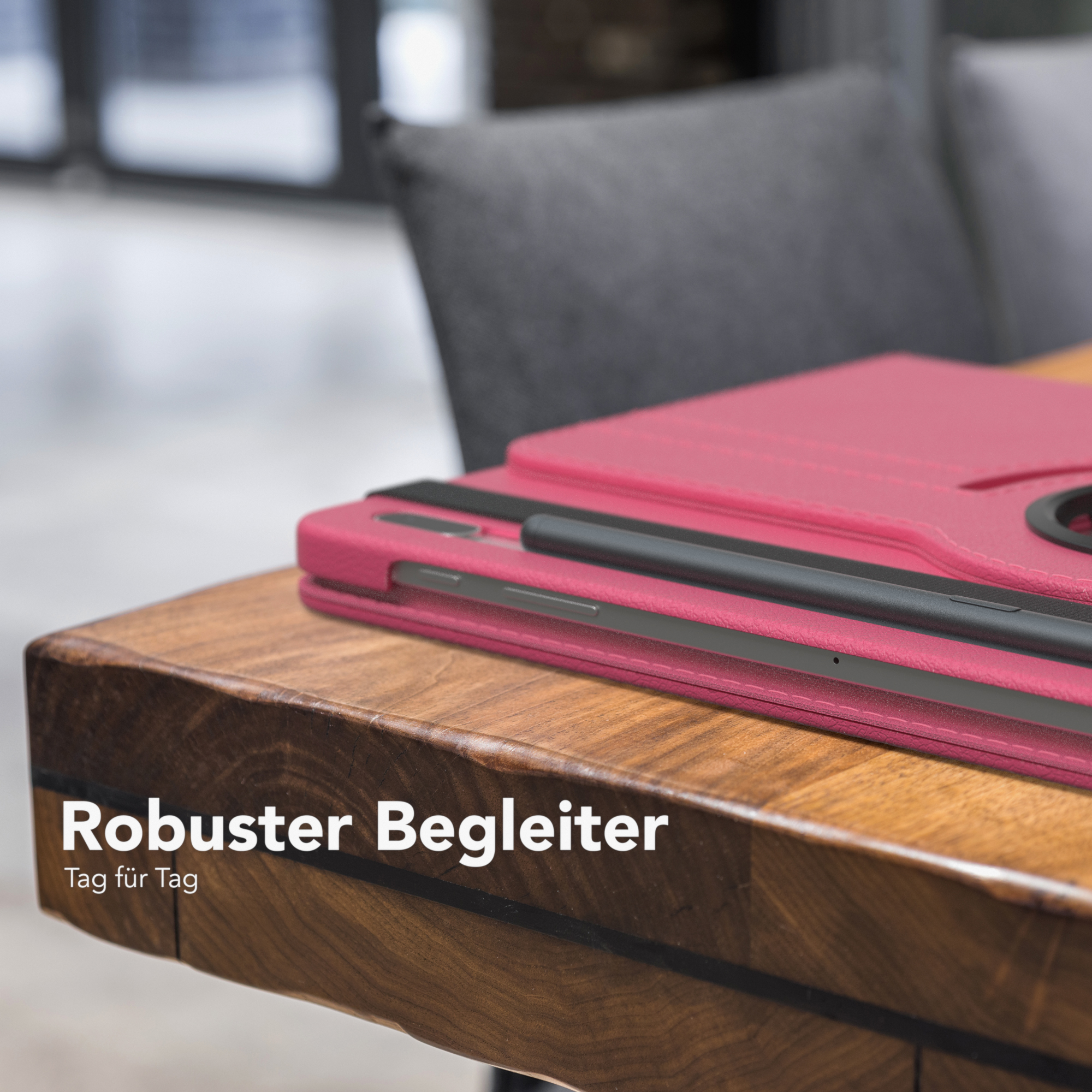 Eine pinke Tablethülle liegt auf einem Holztisch. Ein schwarzer Stift liegt am Rand. Der Text lautet 'Robuster Begleiter'.