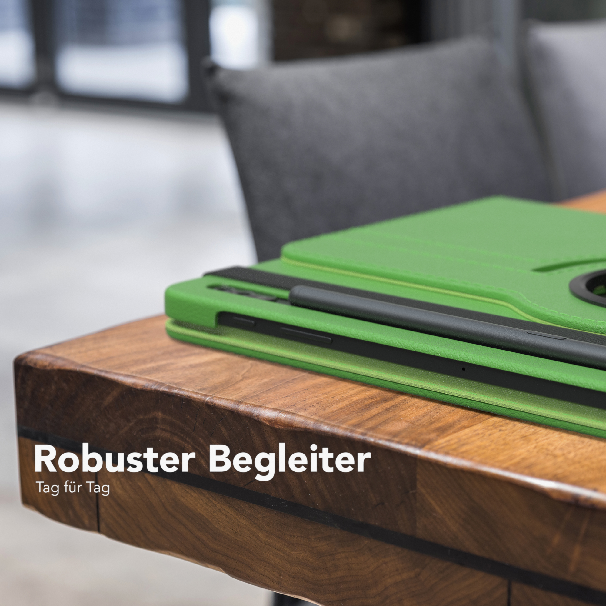Grüne Tablet-Hülle auf Holztisch, grauer Stuhl im Hintergrund.