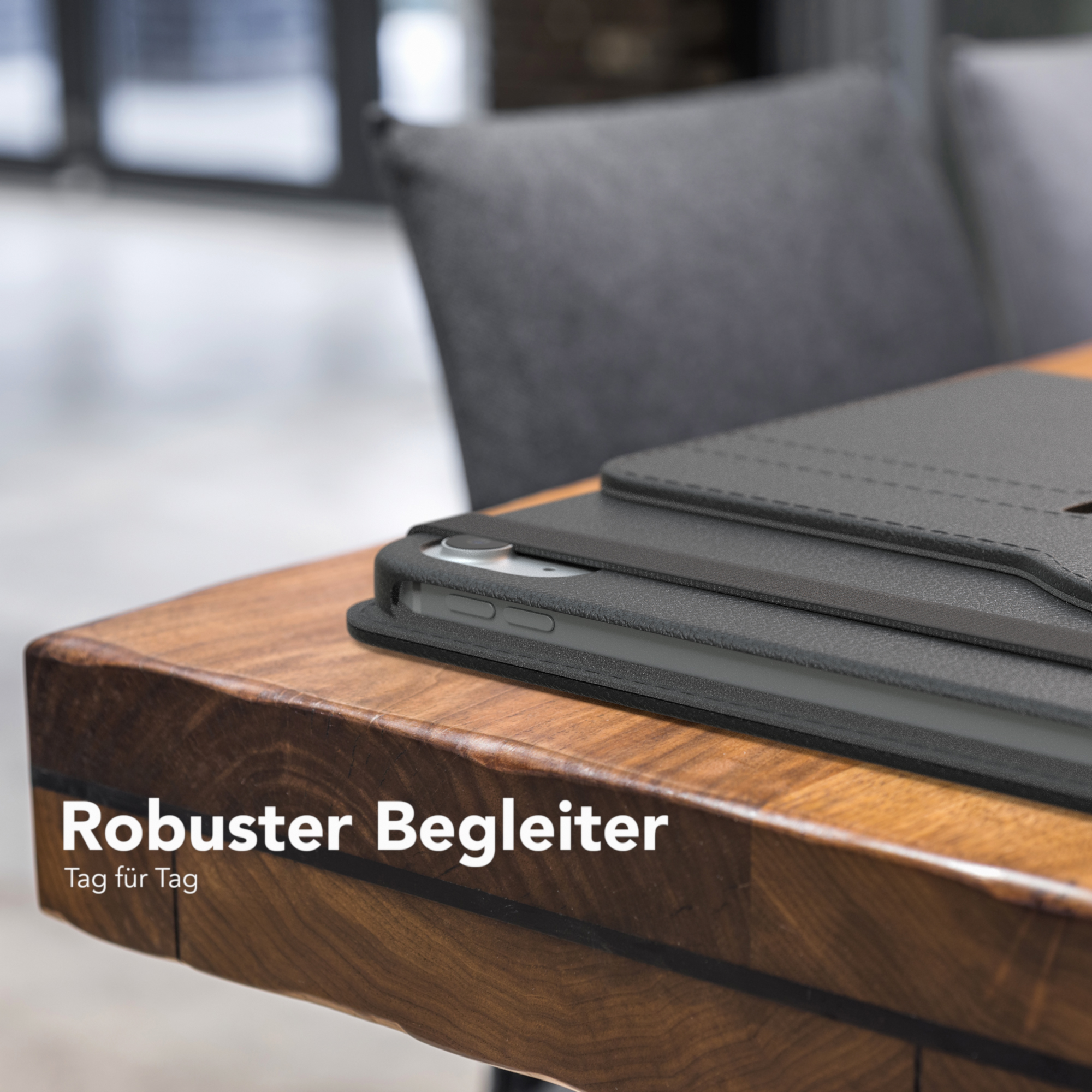 Schwarze Tablethülle auf einem Holztisch. Ein grauer Stuhl im Hintergrund.
