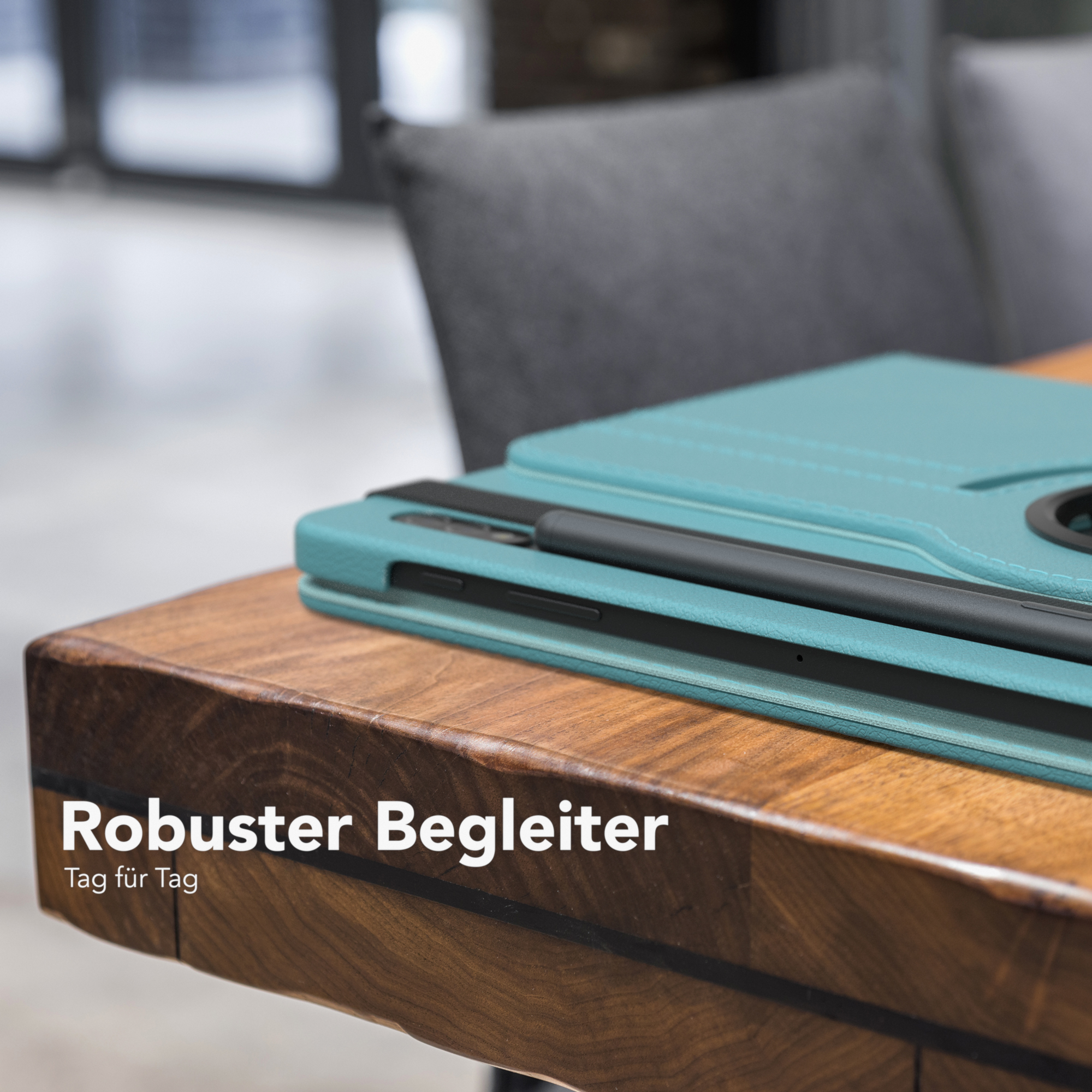 Tablet in einer türkisfarbenen Hülle auf einem Holztisch neben einem Stuhl. Stift sichtbar.