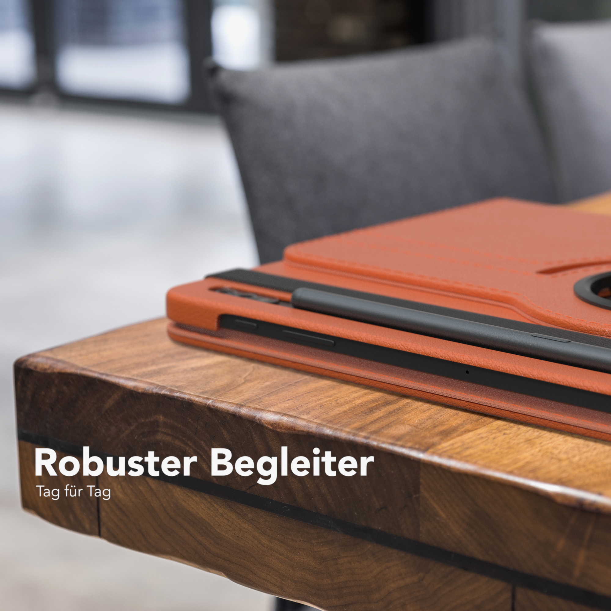Tablet in einer orangefarbenen Hülle auf einem Holztisch. Im Hintergrund ist ein grauer Stuhl teilweise sichtbar.