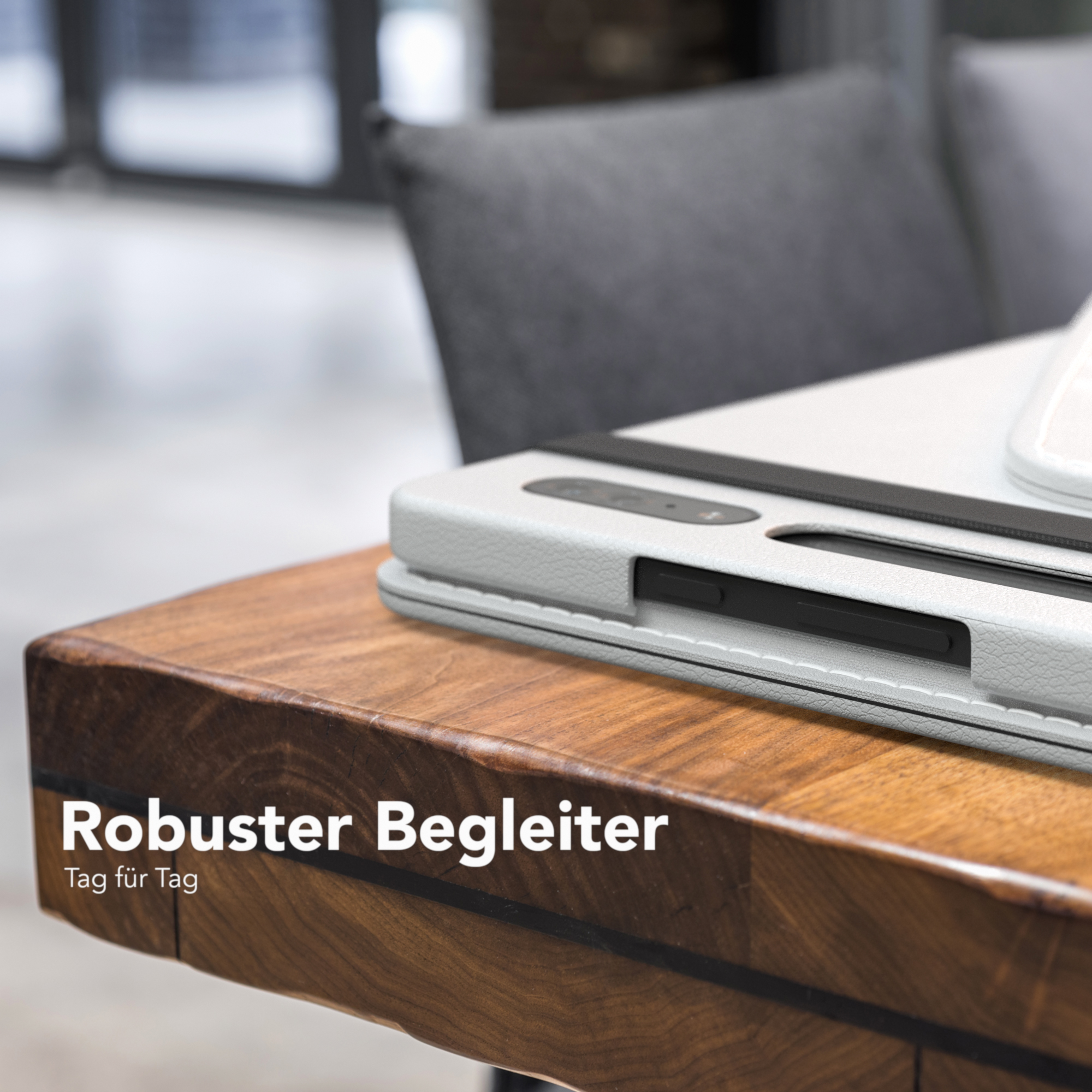 Tablet in weißer Hülle auf Holztisch, Text: Robuster Begleiter Tag für Tag. Grauer Stuhl sichtbar.