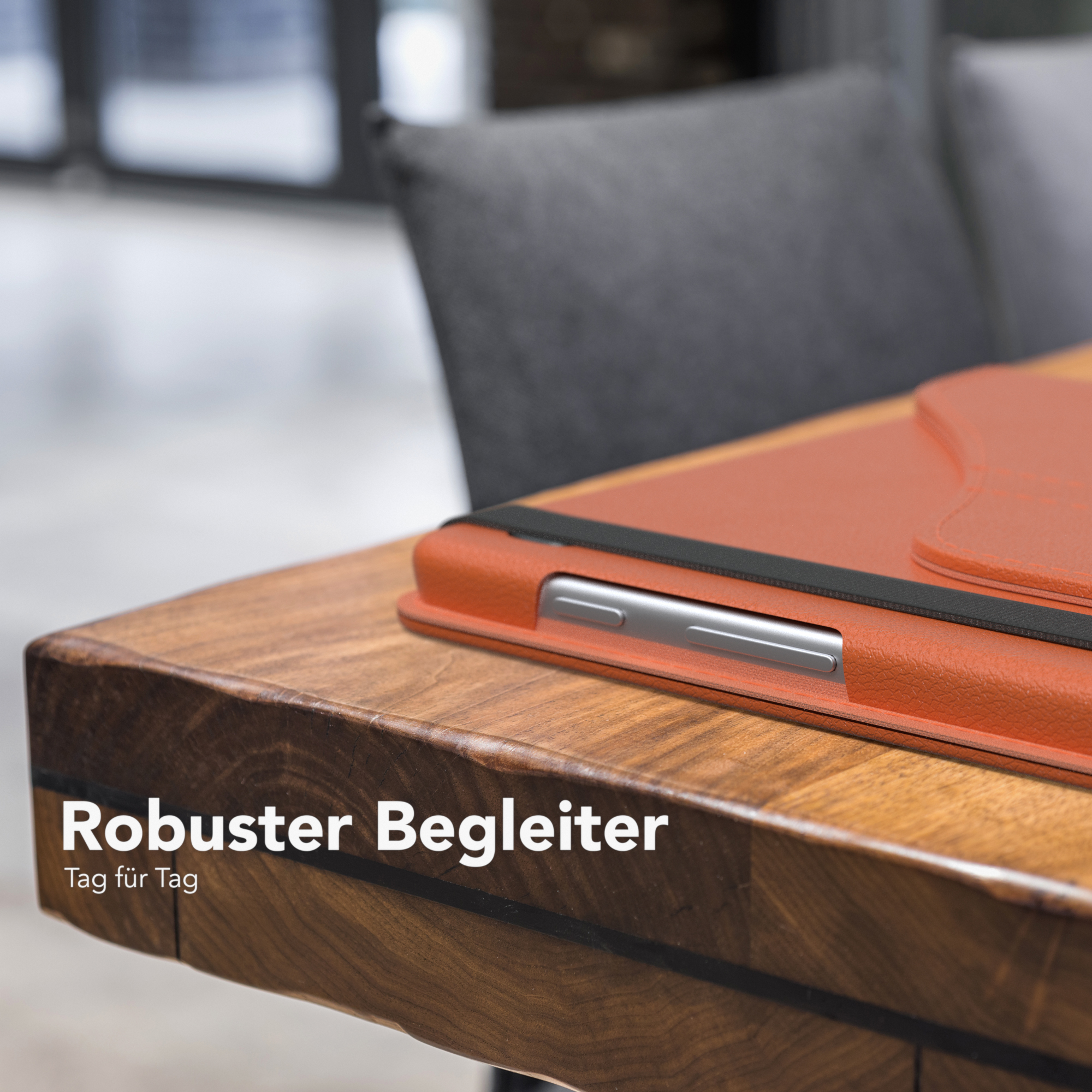 Orangefarbene Tablethülle auf einem Holztisch. Im Hintergrund ein grauer Stuhl.