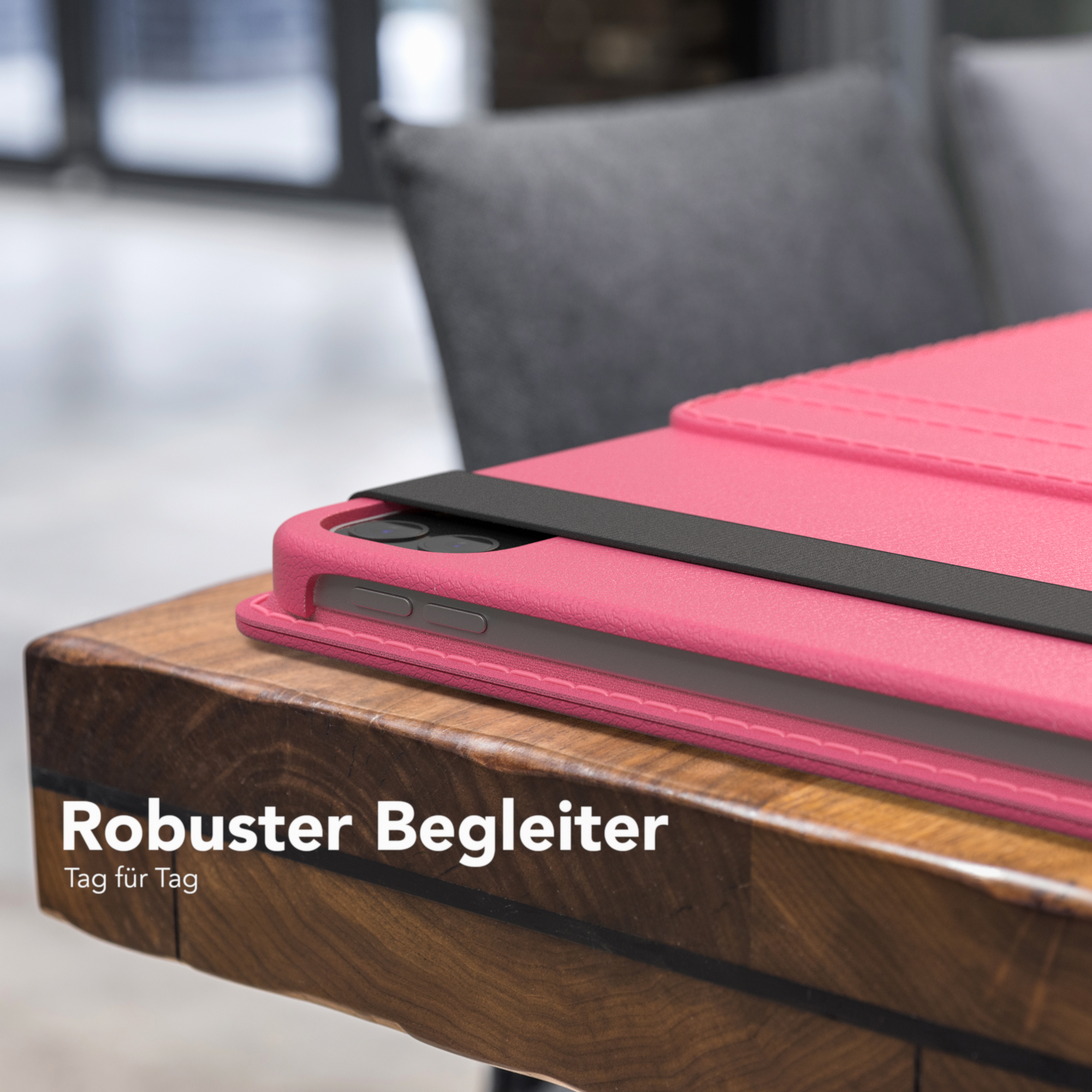 Rosa Tablet-Hülle auf Holztisch. Schwarzer Riemen über der Hülle. Grauer Stuhl im Hintergrund sichtbar.