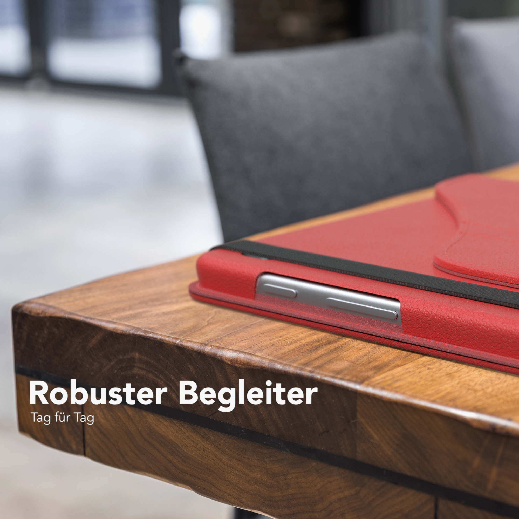 Rote Tablet-Hülle auf einem Holztisch, ein dunkler Stuhl im Hintergrund.